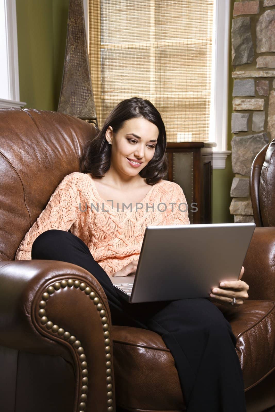 Caucasian/Hispanic young woman sitting in leather chair looking at laptop computer.