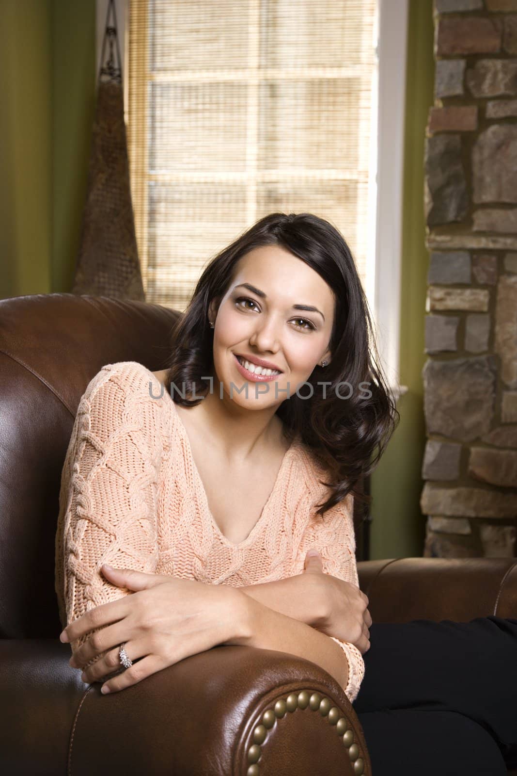 Caucasian/Hispanic young woman sitting in leather chair smiling and looking at viewer.