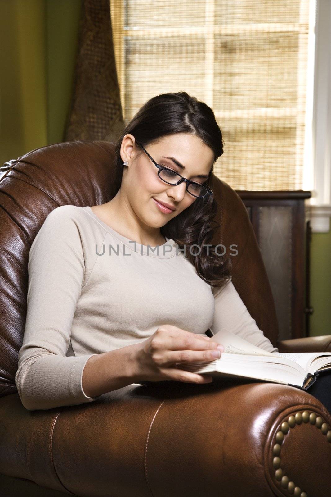 Caucasian/Hispanic young woman sitting in leather chair reading a book.