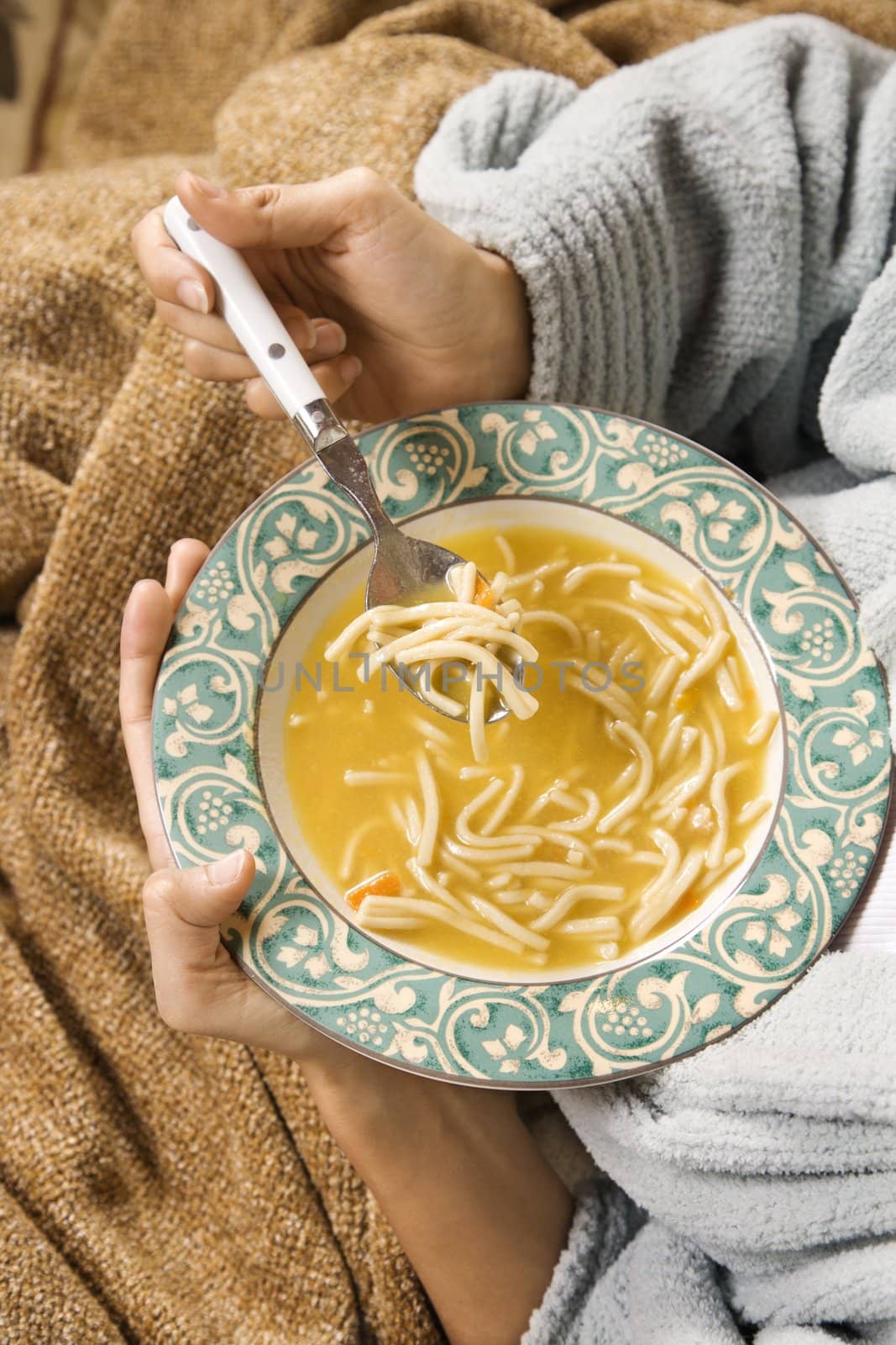 Bowl of chicken noodle soup held in Caucasian/Hispanic hands.