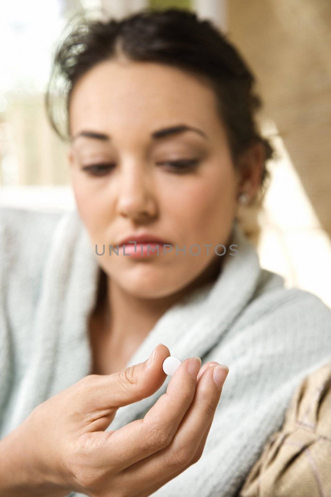 Caucasian/Hispanic young woman in bathrobe holding pill in hand.