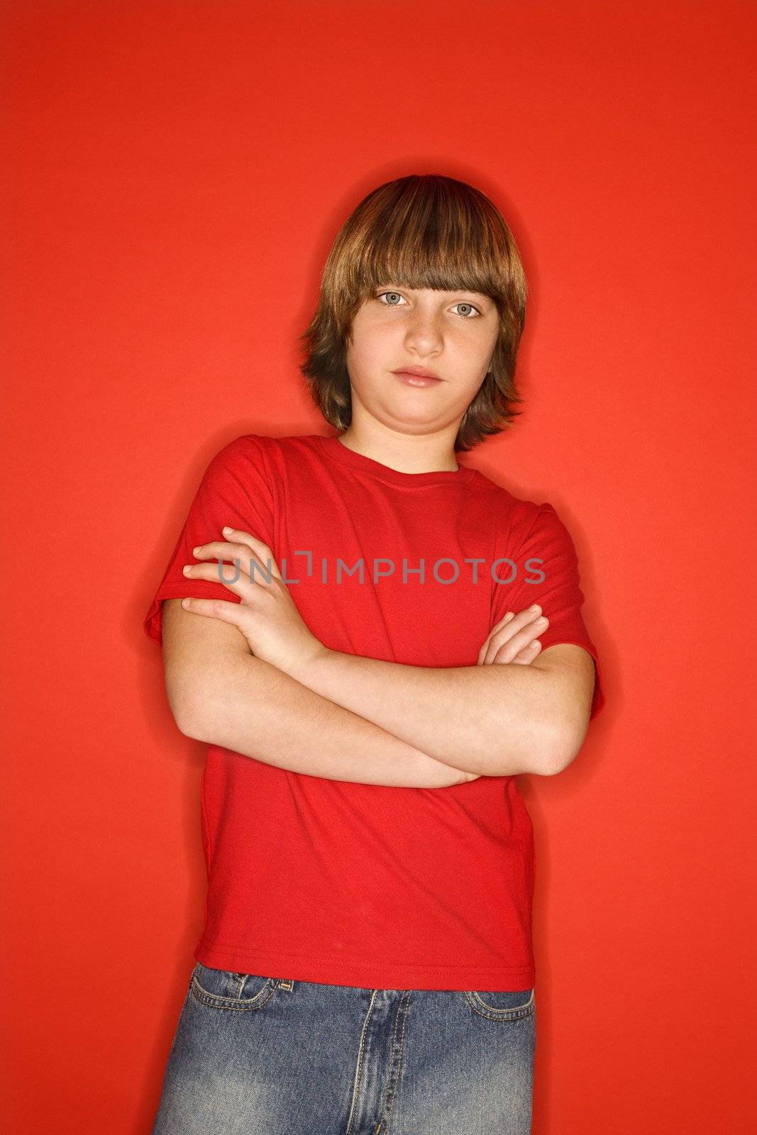 Portait of Caucasian boy with arms crossed standing against red background.