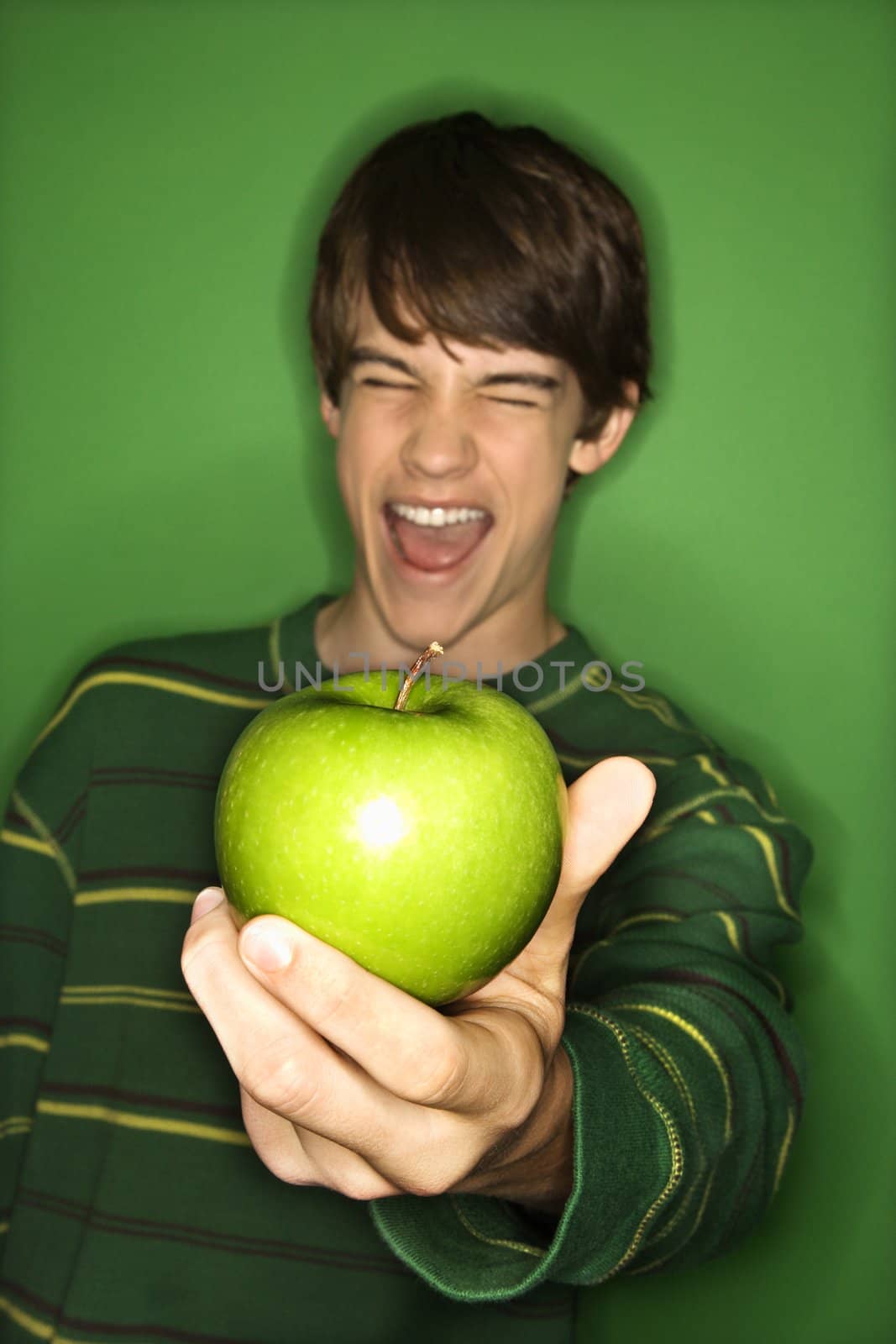 Portrait of Caucasian teen boy holding apple out in hand and making facial expression.