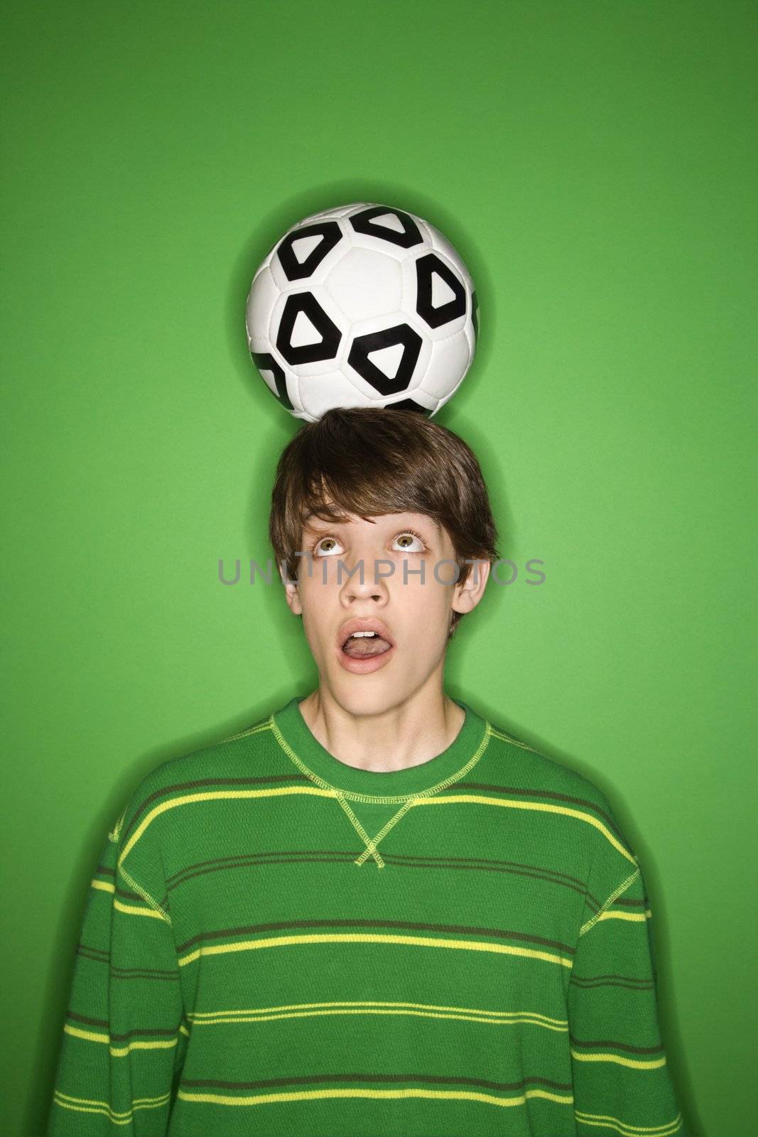 Portrait of Caucasian teen boy balancing soccer ball on head and looking up at it with eyes.
