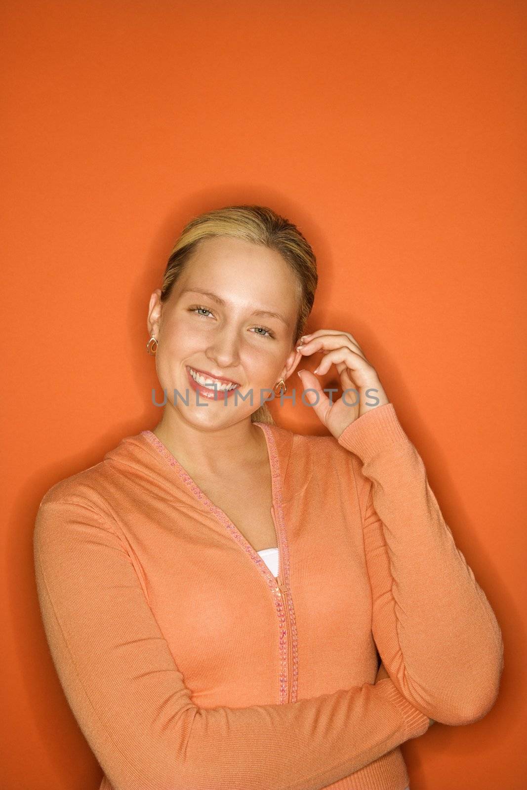 Portrait of smiling blond Caucasian teen girl standing against orange background.