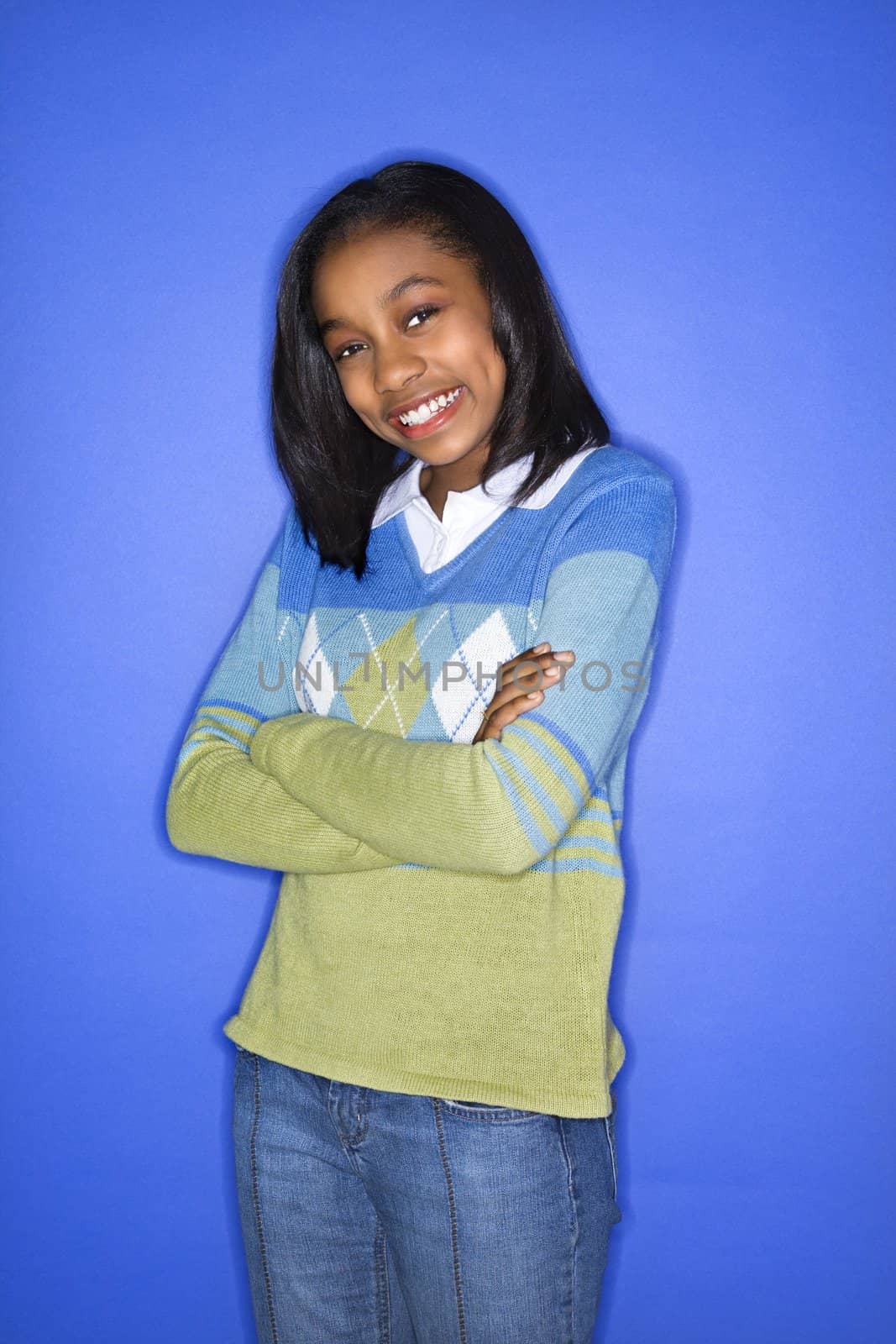 Portrait of African-American teen girl with arms crossed standing against blue background.