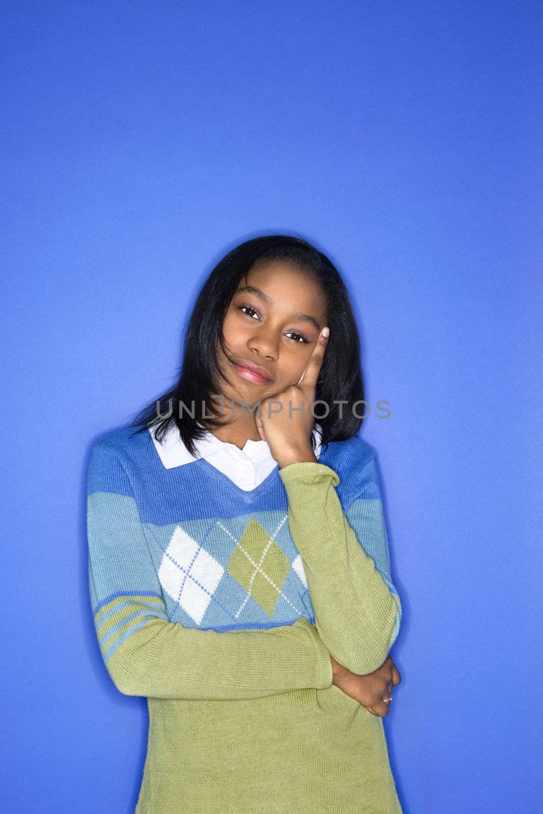 Portrait of African-American teen girl with head on hand standing against blue background.