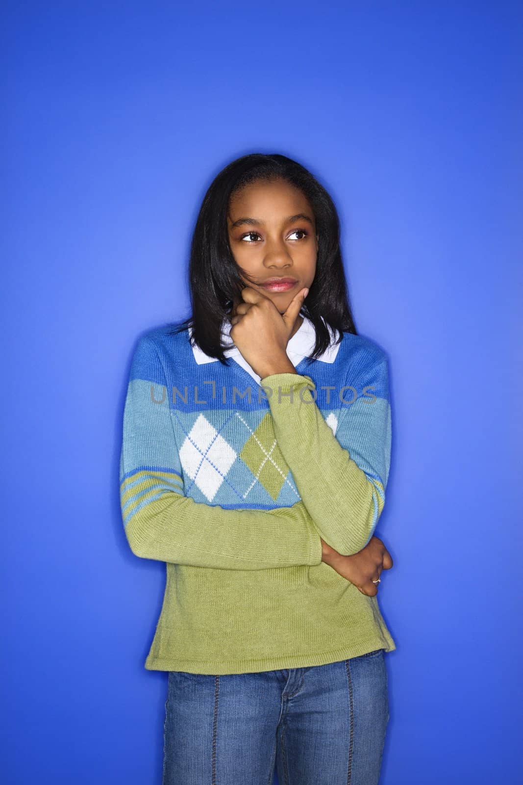 Portrait of African-American girl with hand on chin standing in front of blue background.
