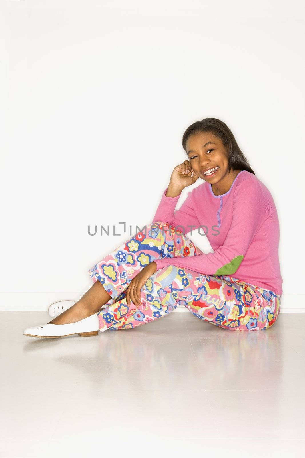 Portrait of African-American teen girl sitting on floor looking at viewer smiling against white background.