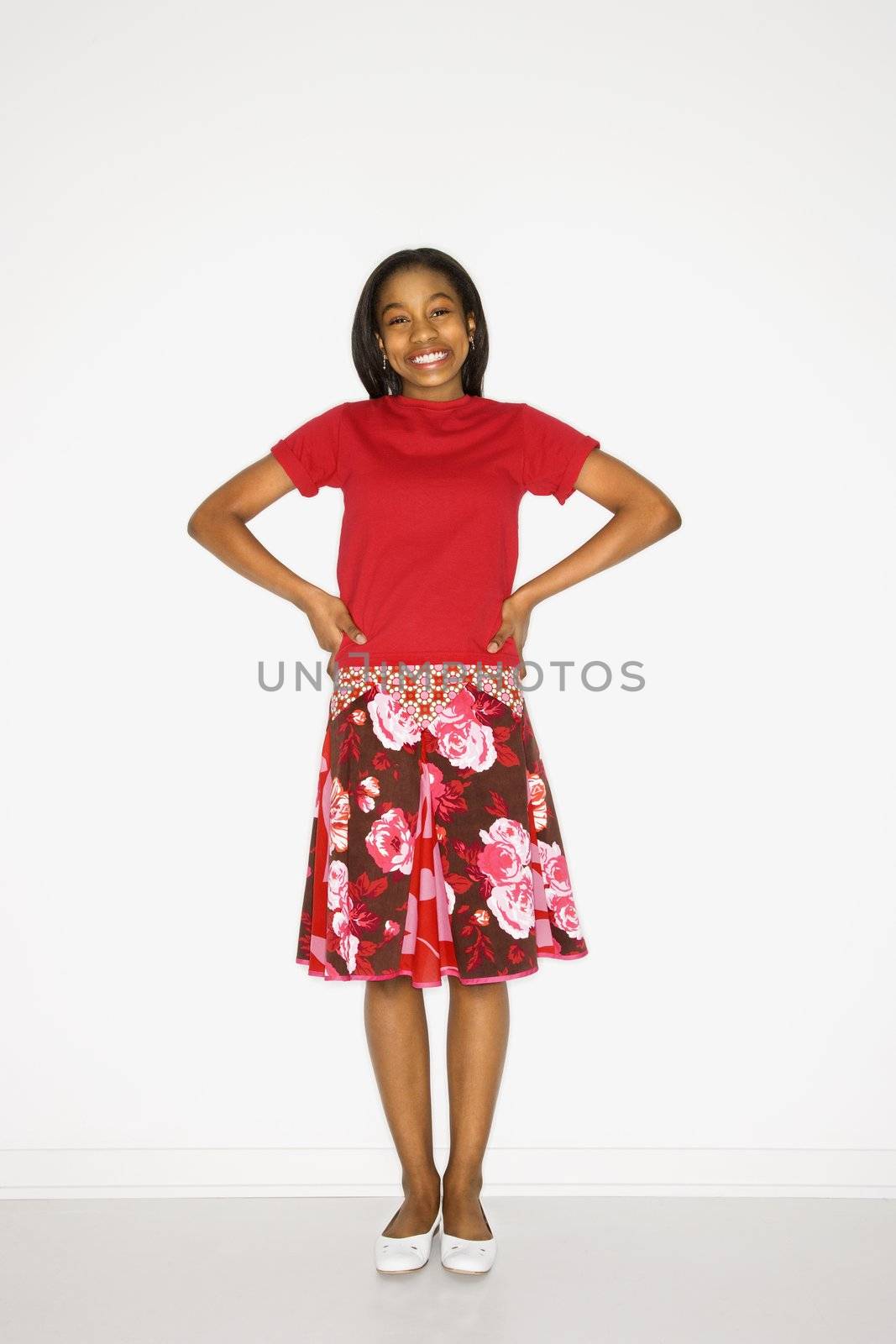 Portrait of African-American teen girl standing with hands on her hips against white background.