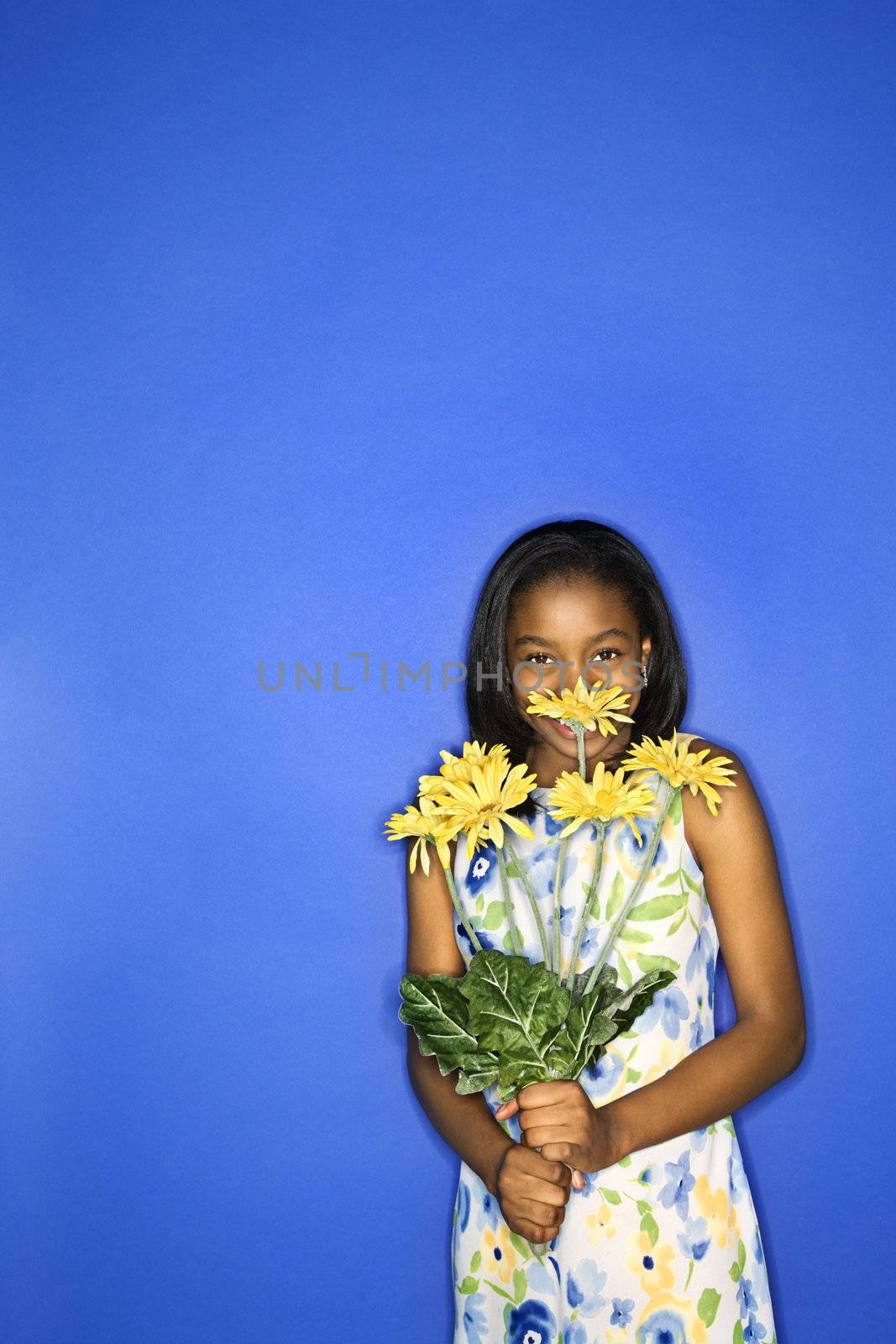 Portrait of African-American teen girl holding a bouquet of daisies in front of blue background.