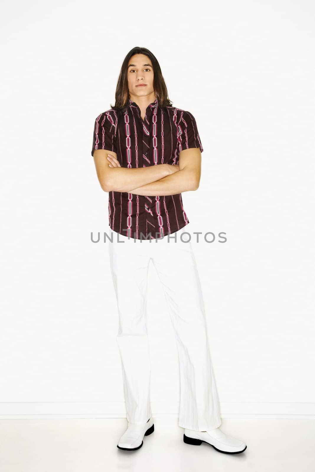 Portrait of Asian-American teen boy standing with arms crossed in front of white background.