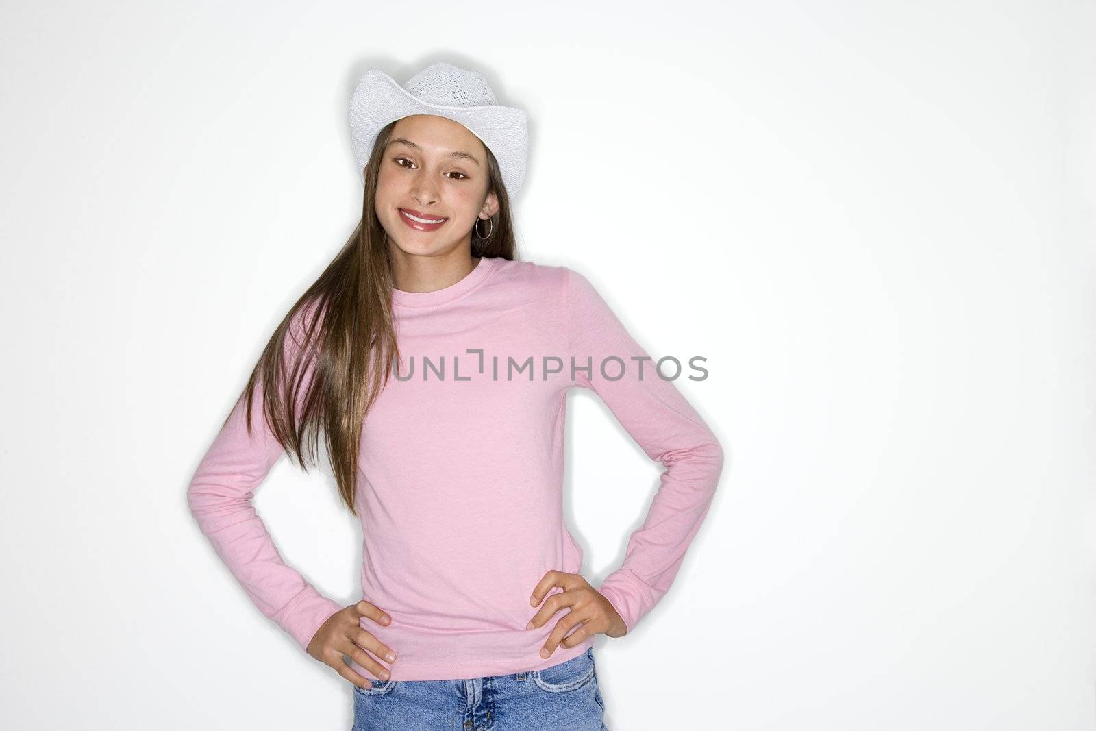 Portrait of Asian-American teen girl with cowboy hat and hands on hips standing in front of white background.