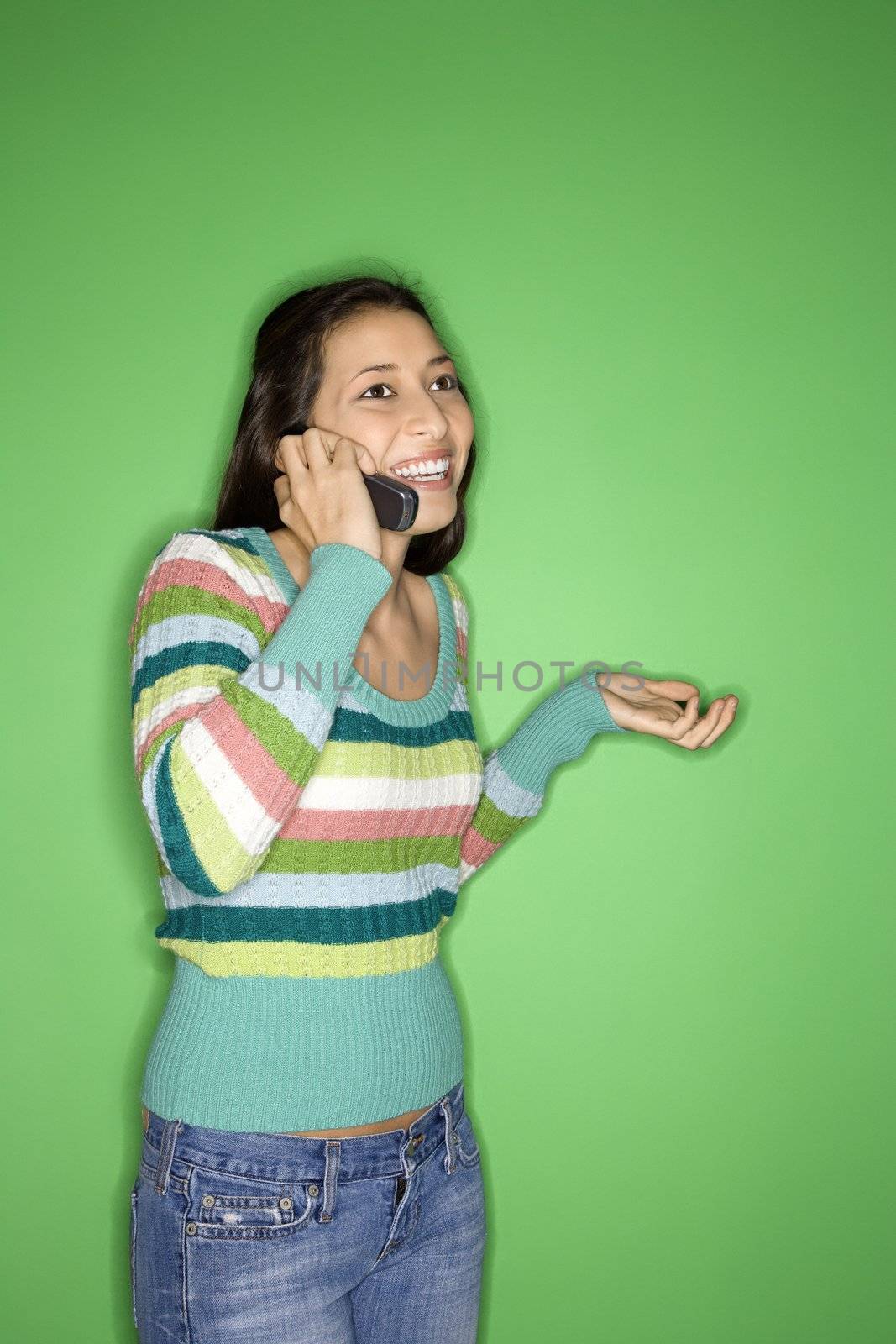 Portrait of Multi-racial teen girl talking on cellphone and smiling standing against green background.