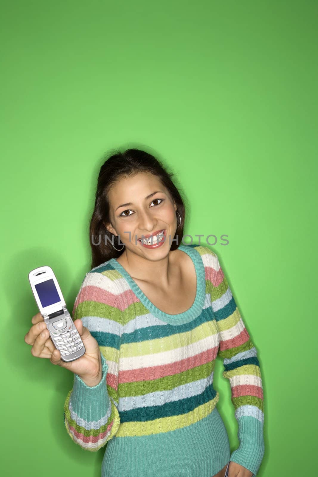 Portrait of smiling Multi-racial teen girl holding cellphone out standing in front of green background.