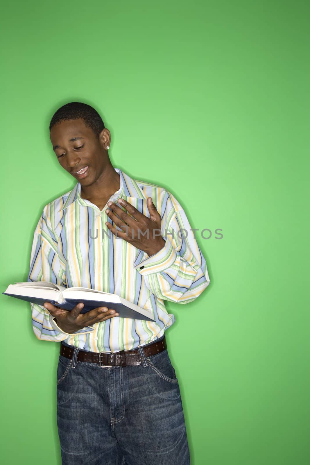 Portrait of African-American teen boy reading book standing in front of green background.