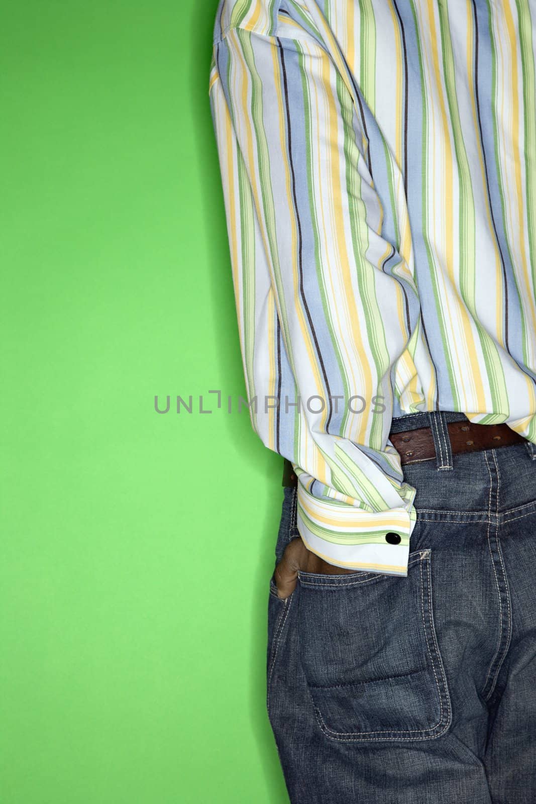 Back view torso of African-American teen boy with hand in back pocket of jeans standing against green background.
