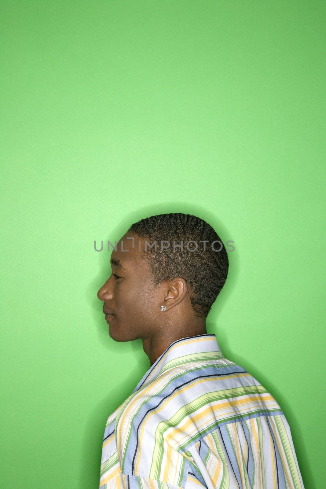 Side view portrait of African-American teen boy against green background.