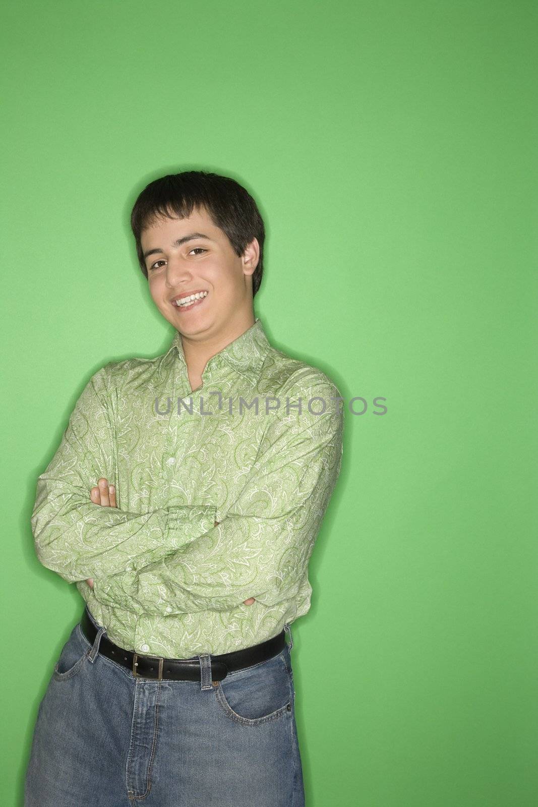 Portrait of Caucasian teen boy smiling with crossed arms standing against green background.l