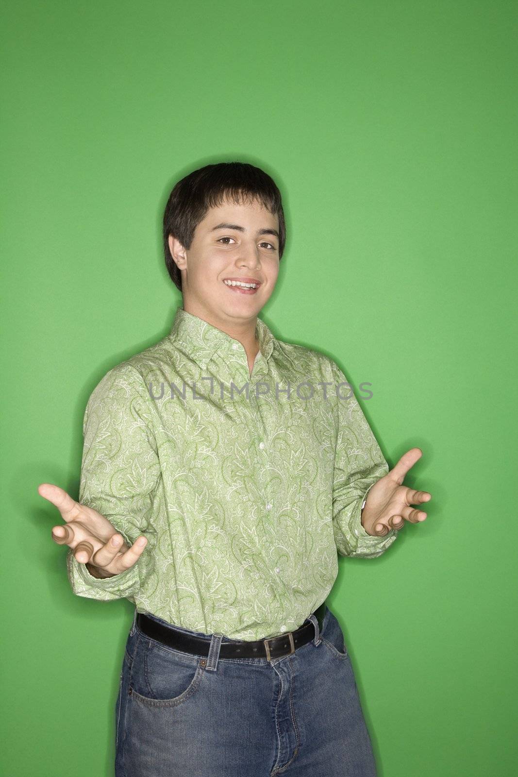 Portrait of Caucasian teen boy with hands opened towards viewer standing against green background.