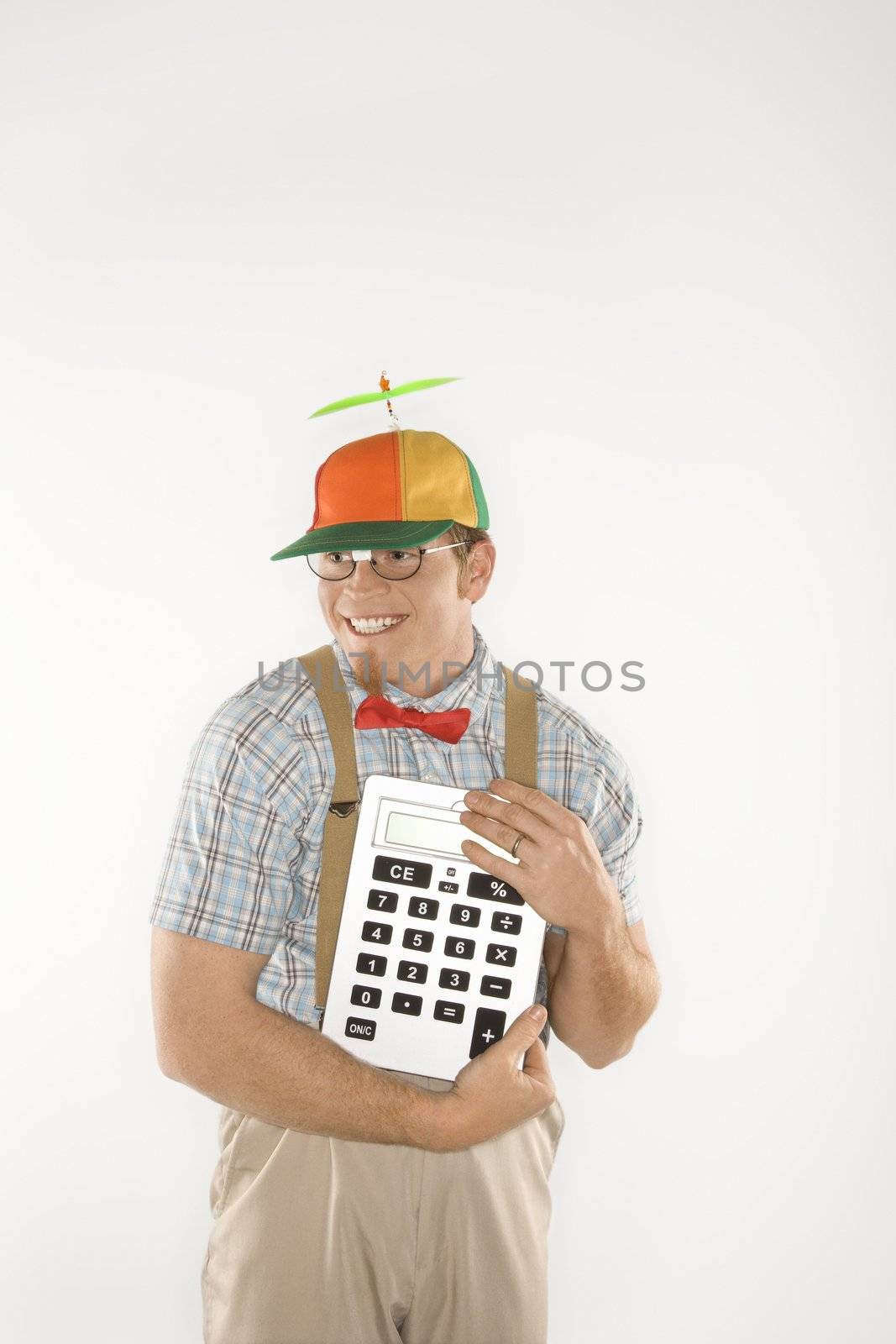 Caucasian young man dressed like nerd wearing beanie and smiling while holding large calculator.