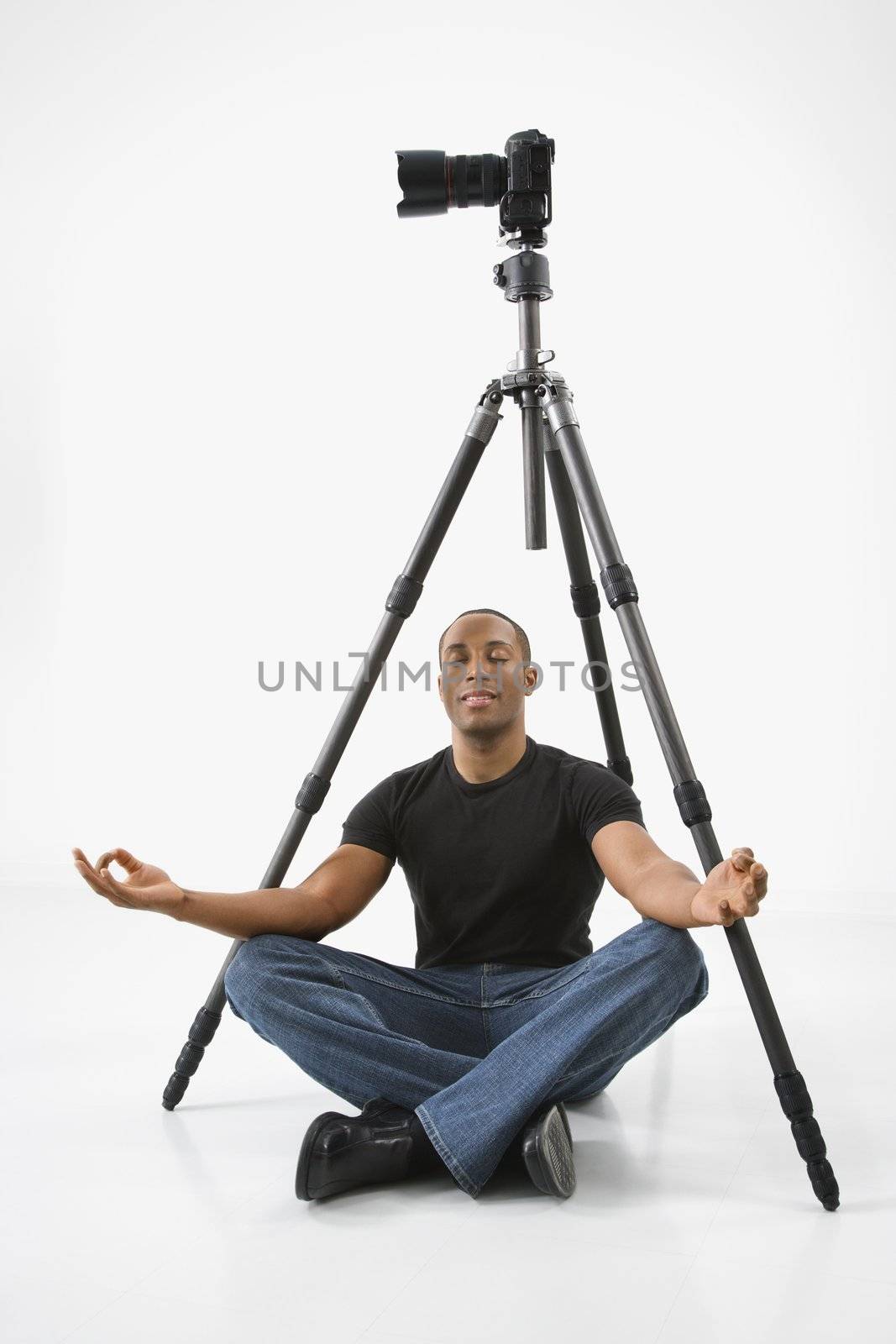 African American young male adult sitting meditating under camera and tripod.