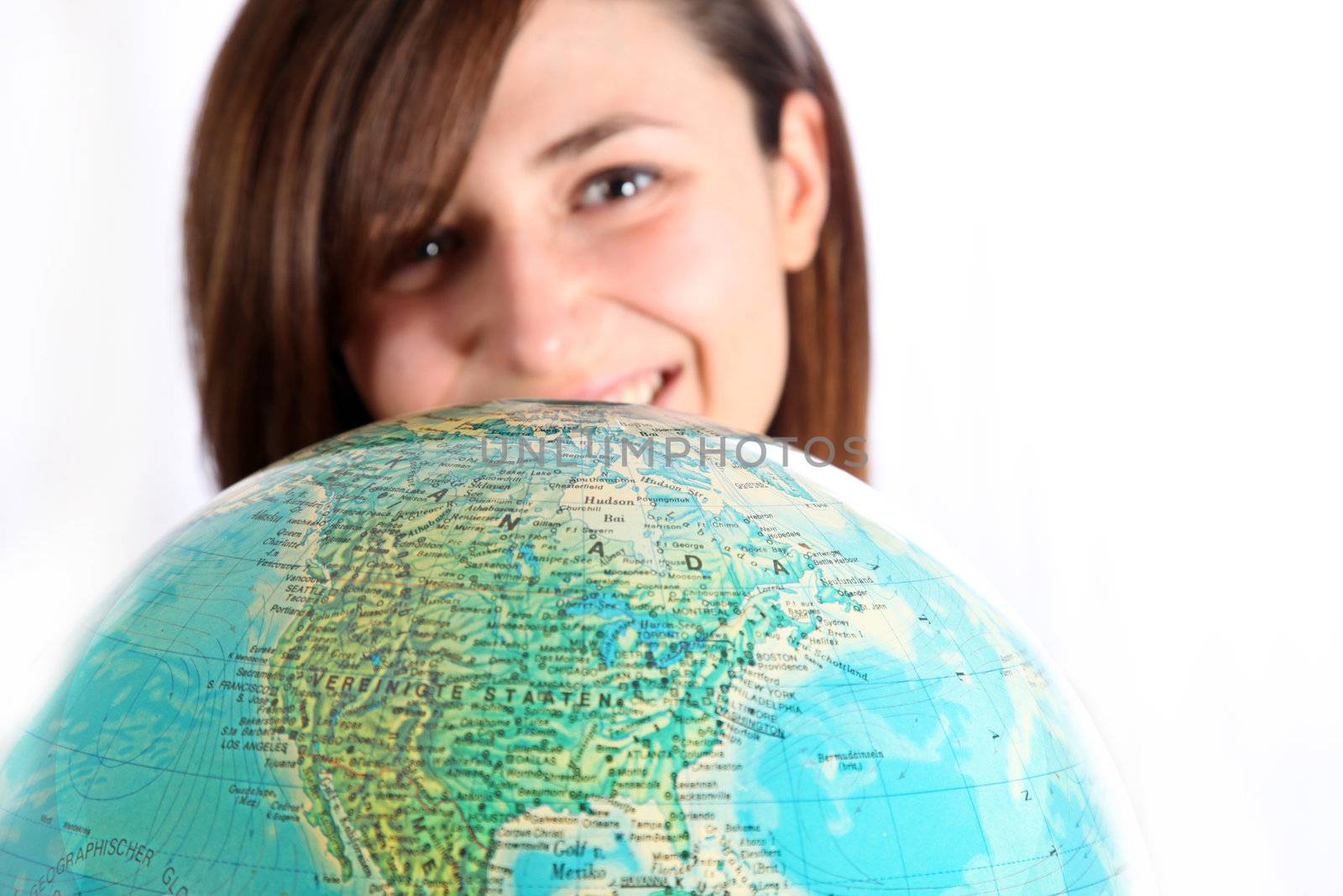 Smiling woman looking over a globe. The globe is in the foreground, the woman in the background out of focus.