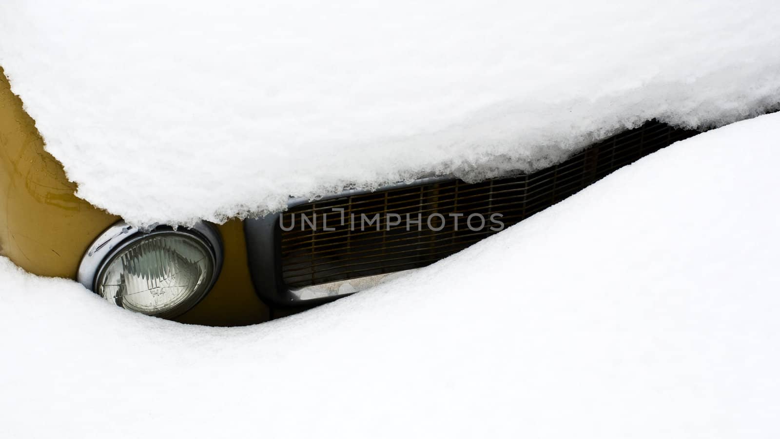 The front and headlight of a car covered in snow