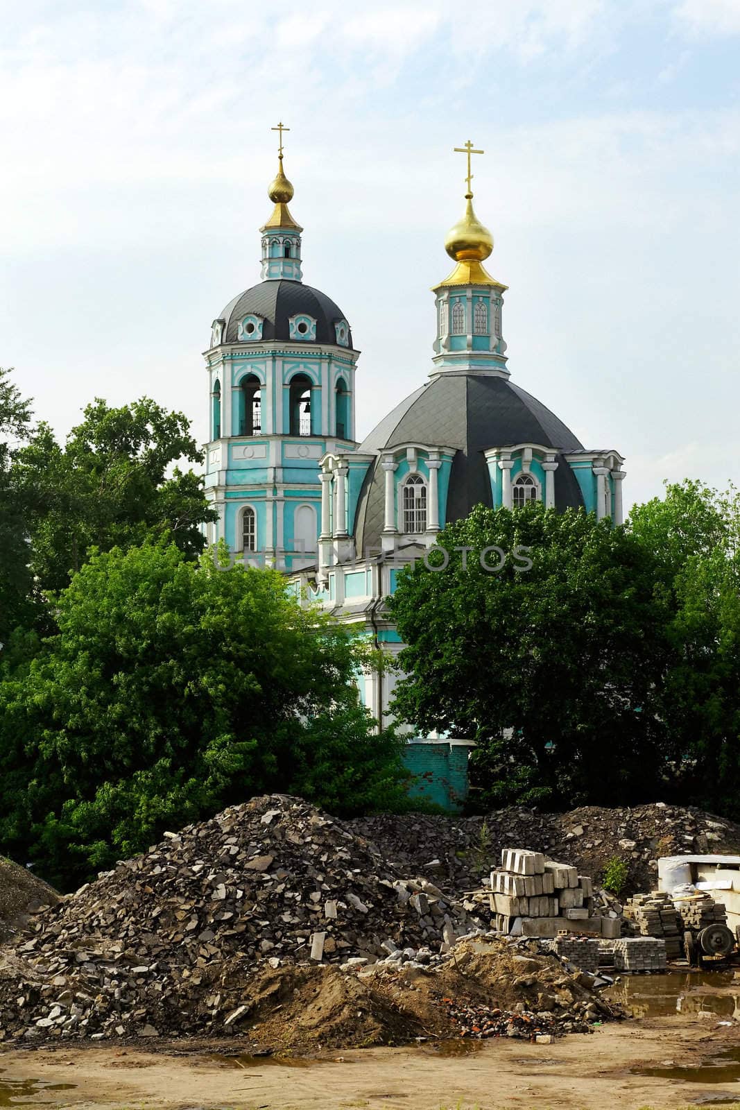 a photo of an Orthodox Church with green walls and golden domes stand behind the trees