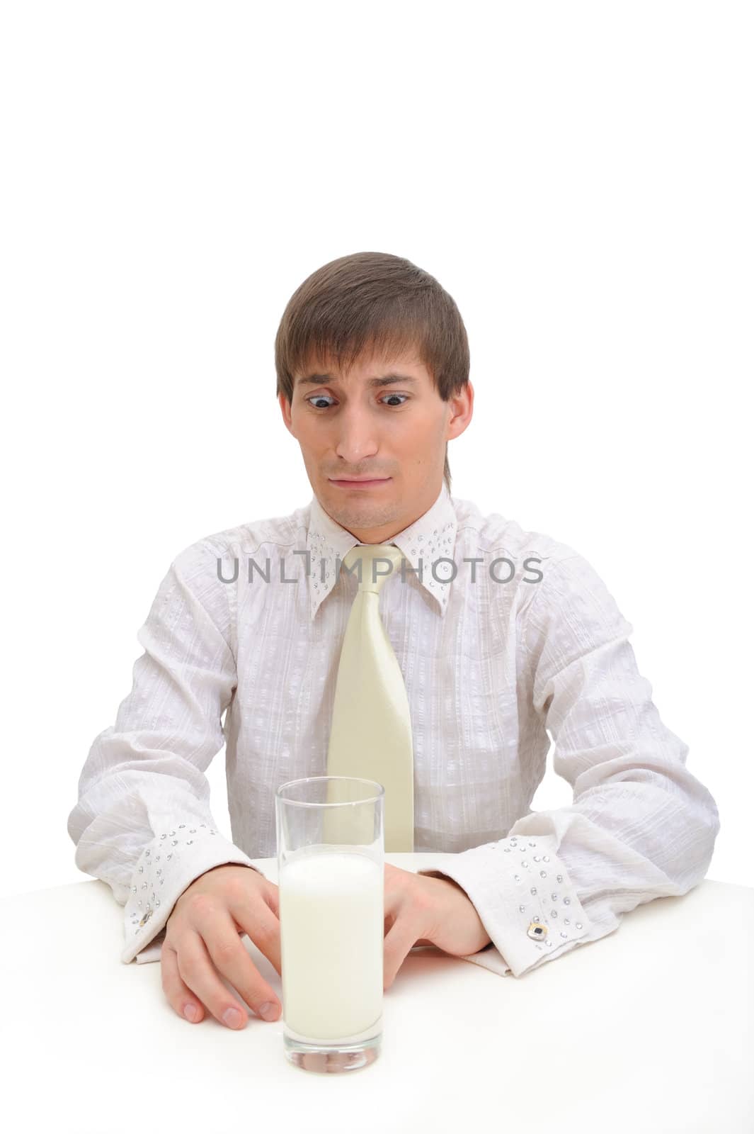 Young handsome  confident  man on white background. He sits for white table and does not want to drink milk from glass.