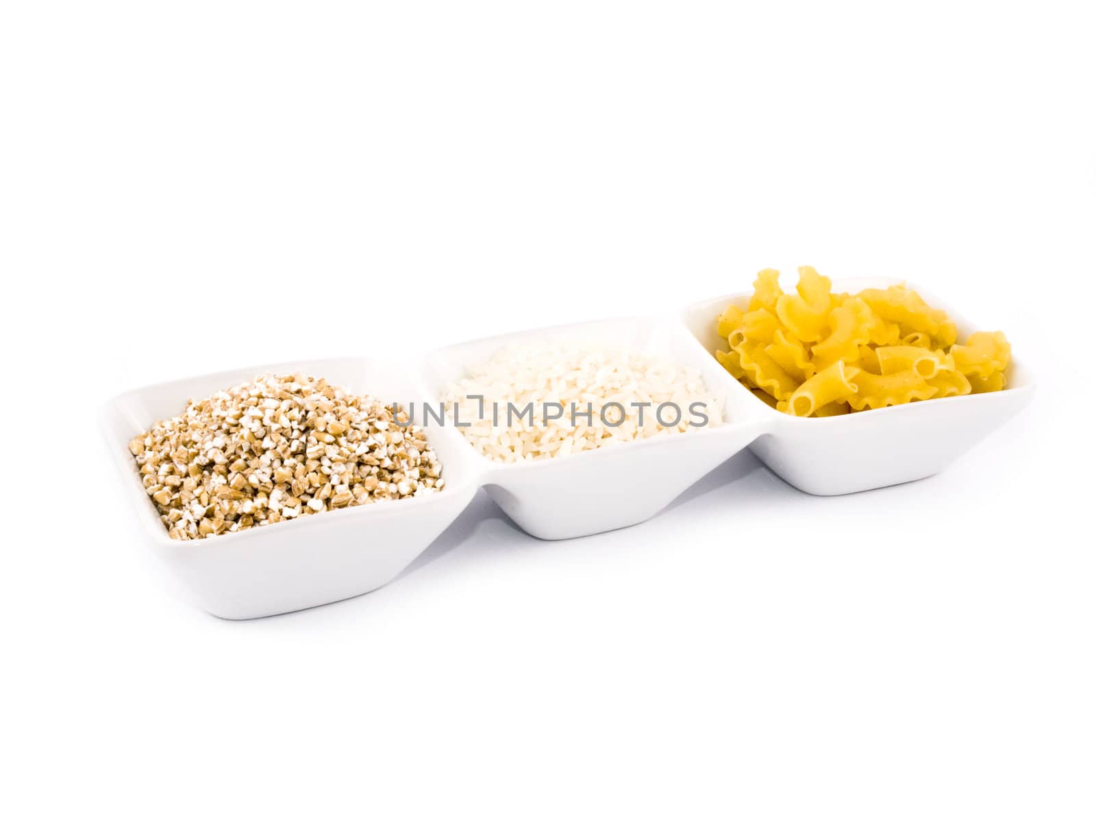 Three porceline bowls filled with pasta, groats and rice, on white background