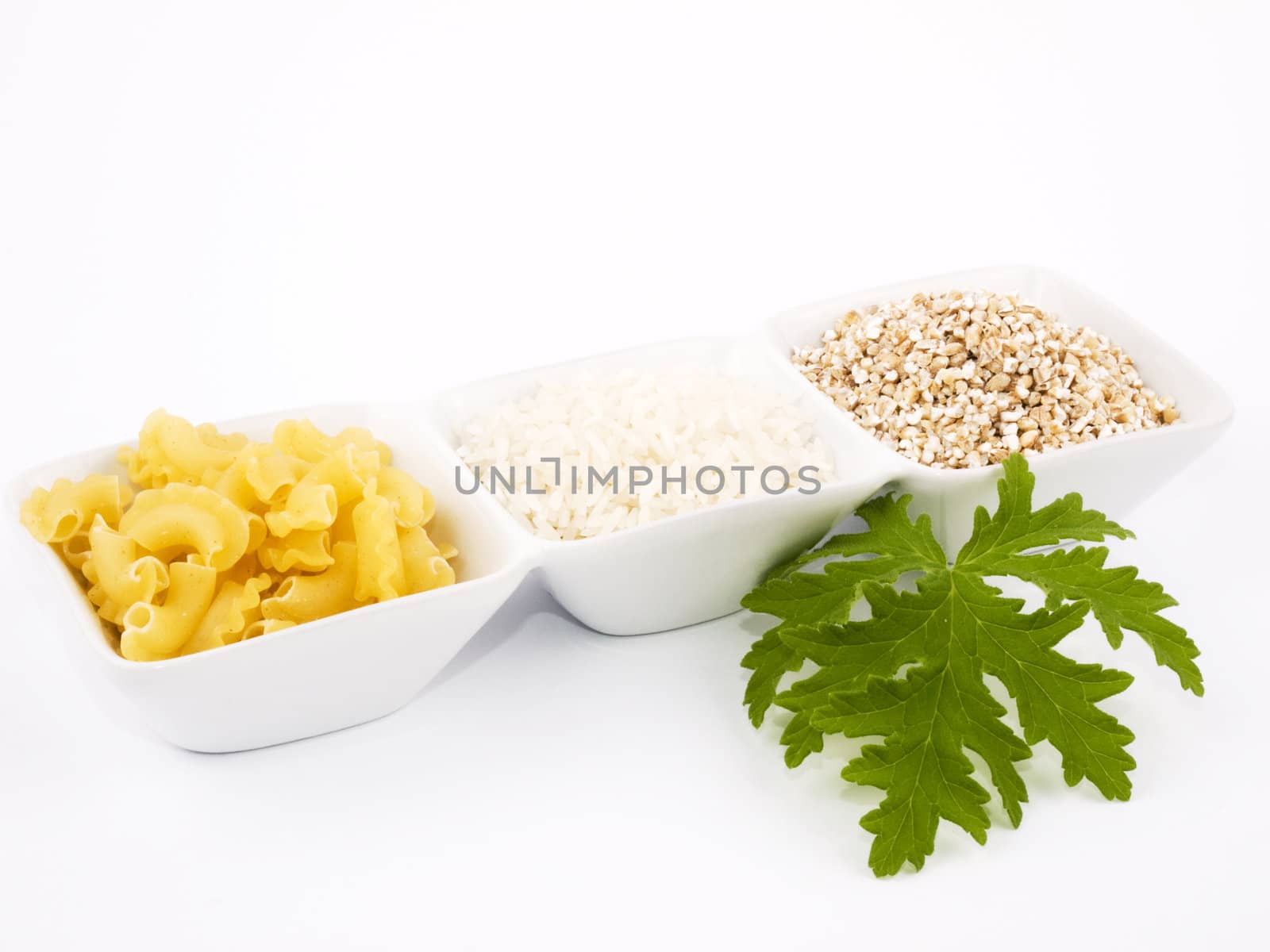 Three porceline bowls filled with pasta, groats and rice, on white background