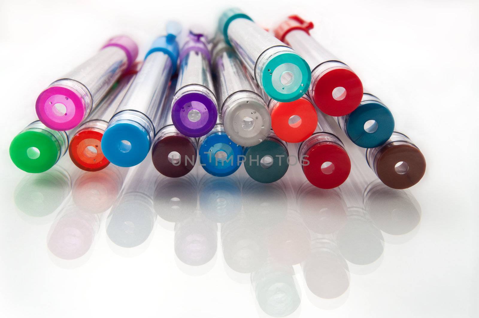 Close and low level angle capturing the ends of many assorted coloured gel pens arranged on a white reflective surface.