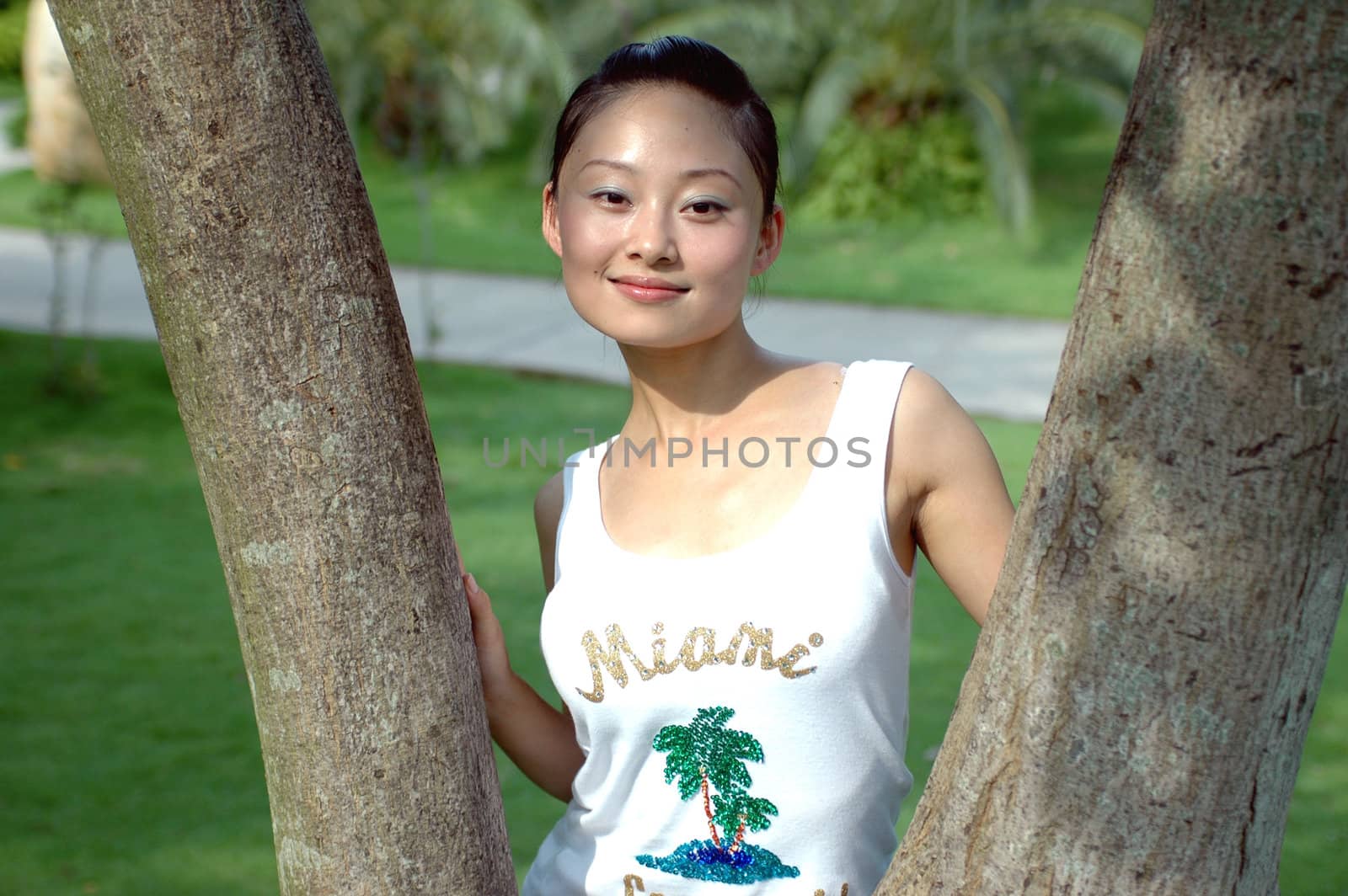 Chinese girl in park standing between two branches, smiling.