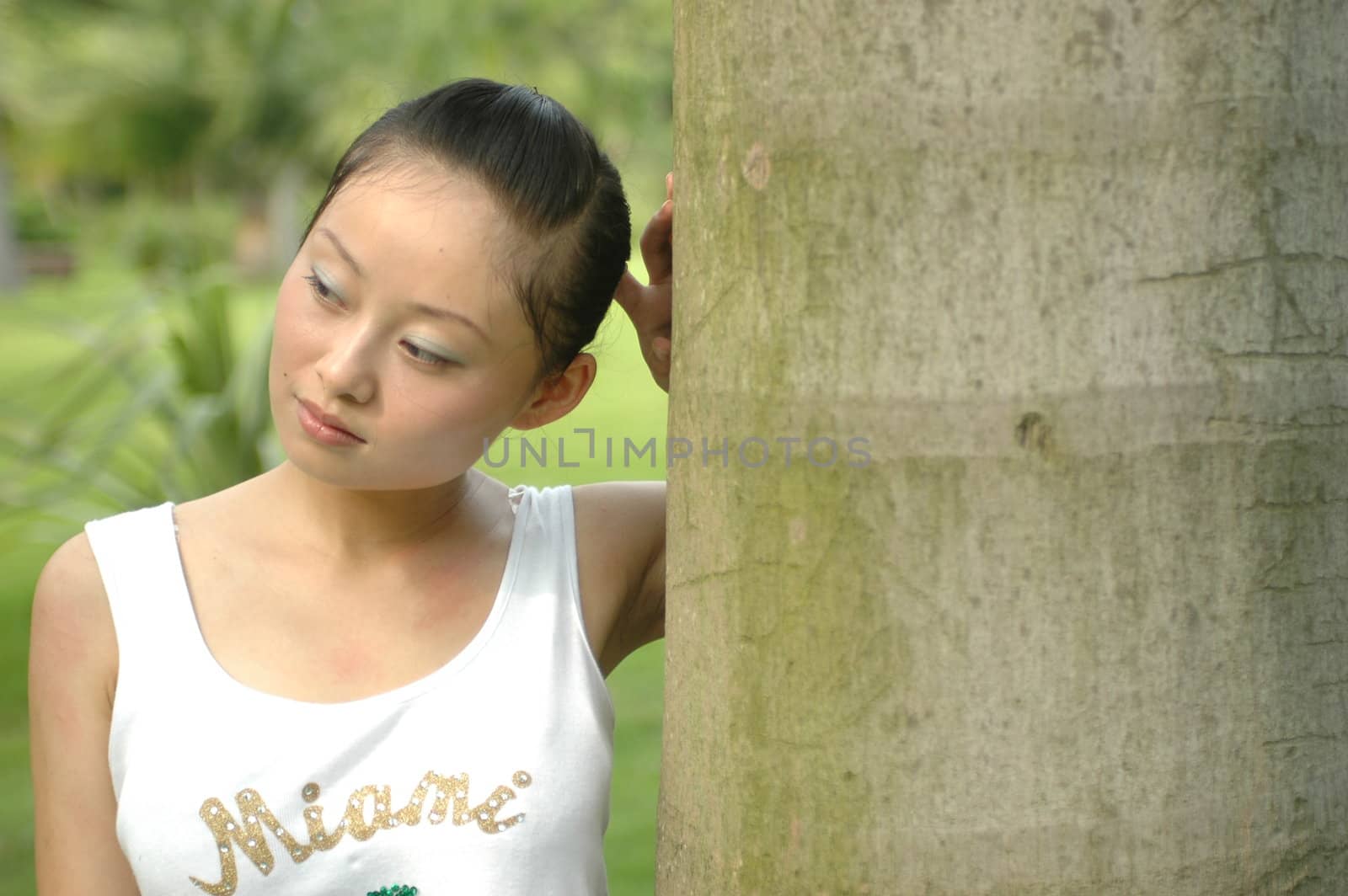 Thoughtful girl standing near palm tree in Chinese park.