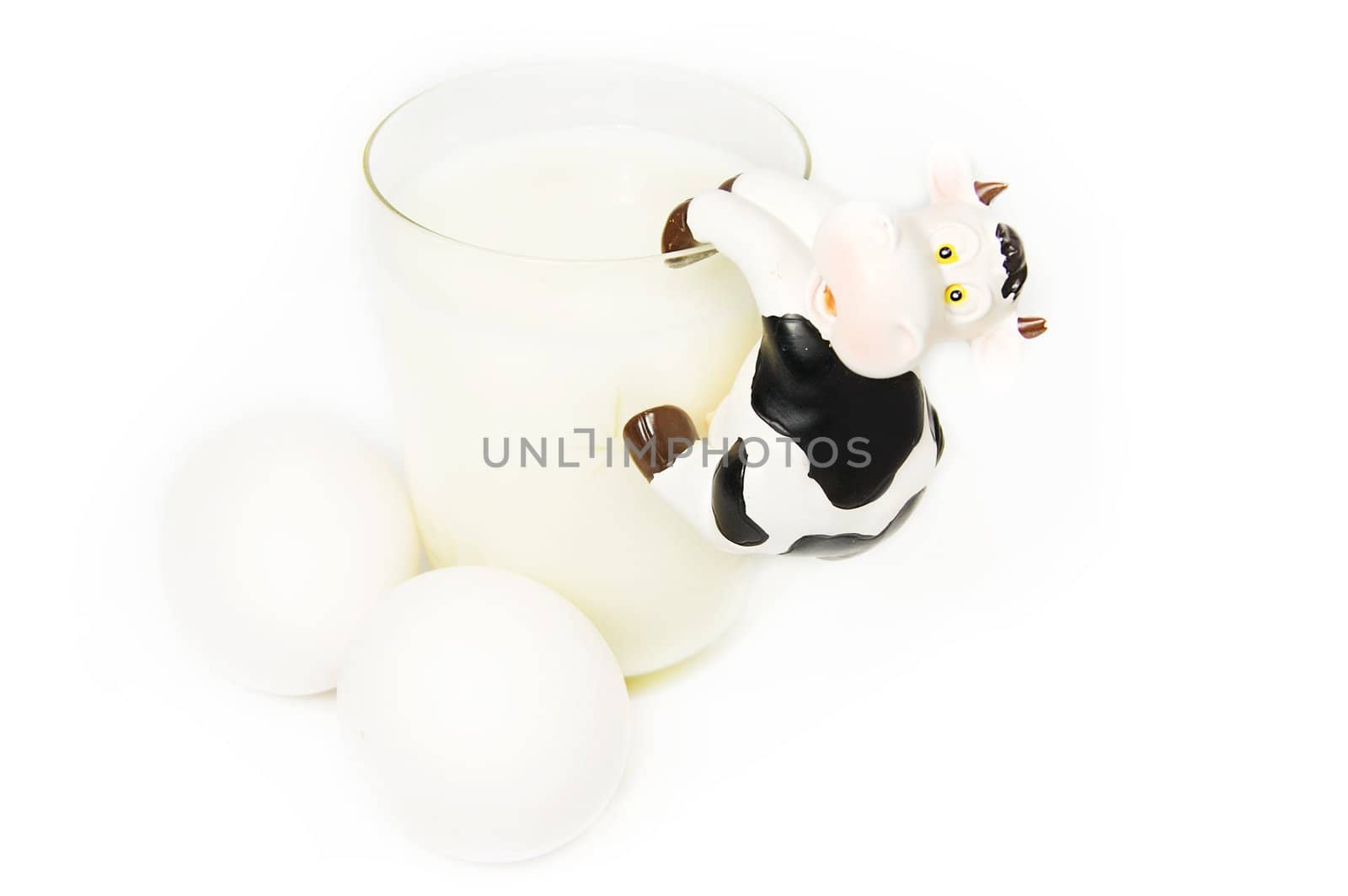 Glass of milk, eggs and toy cow on white