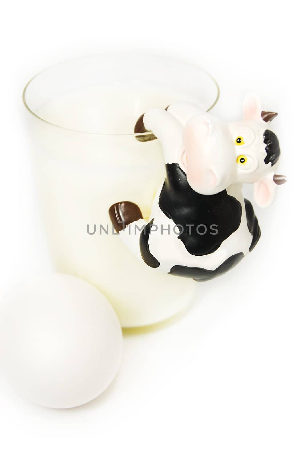 Glass of milk, eggs and toy cow on white