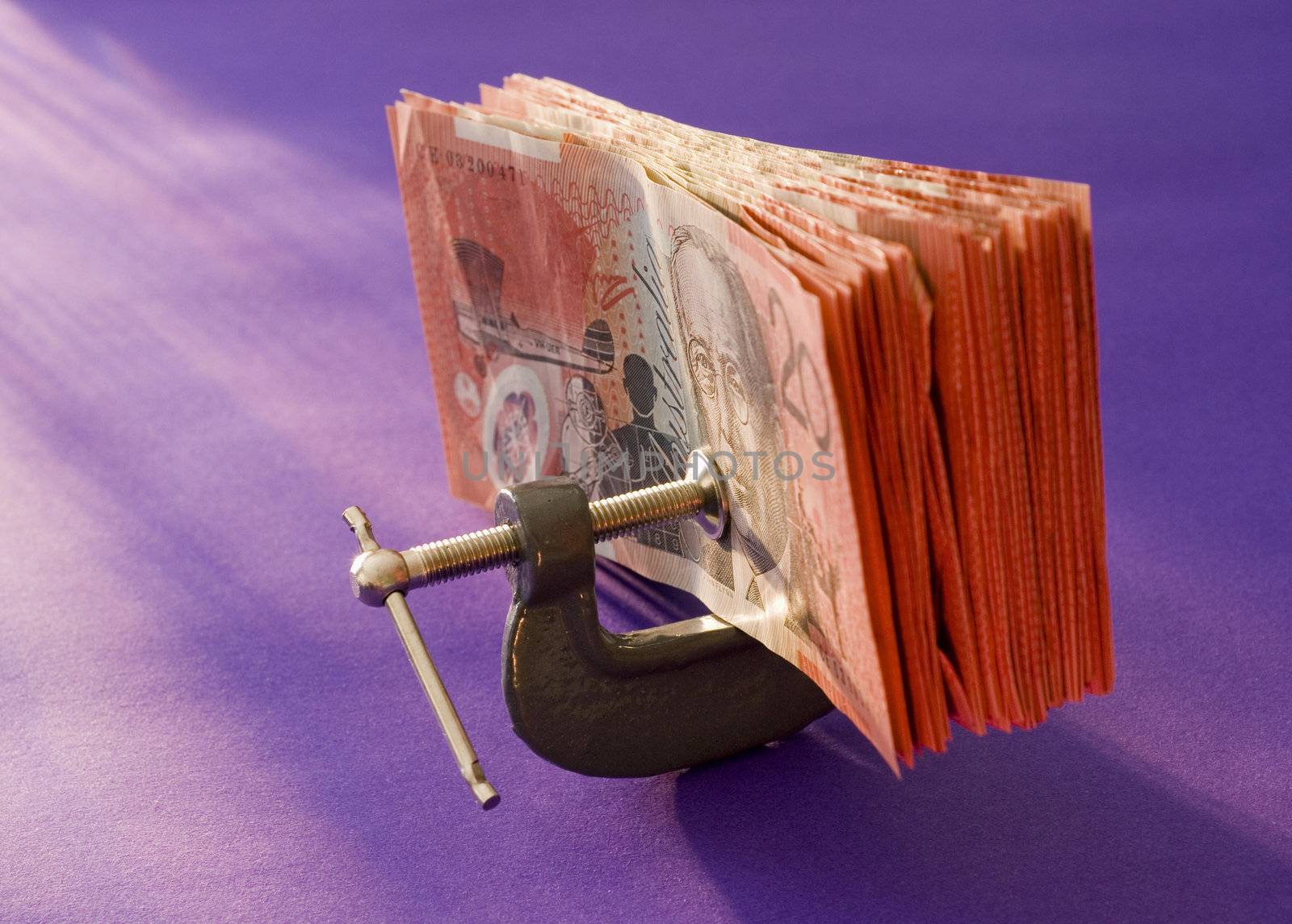 a wad of australian 20 dollar notes pressed in a G clamp