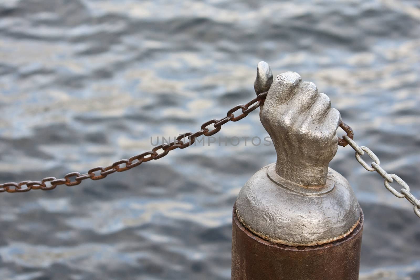 Steel hand holding chain against the water of a lake or ocean