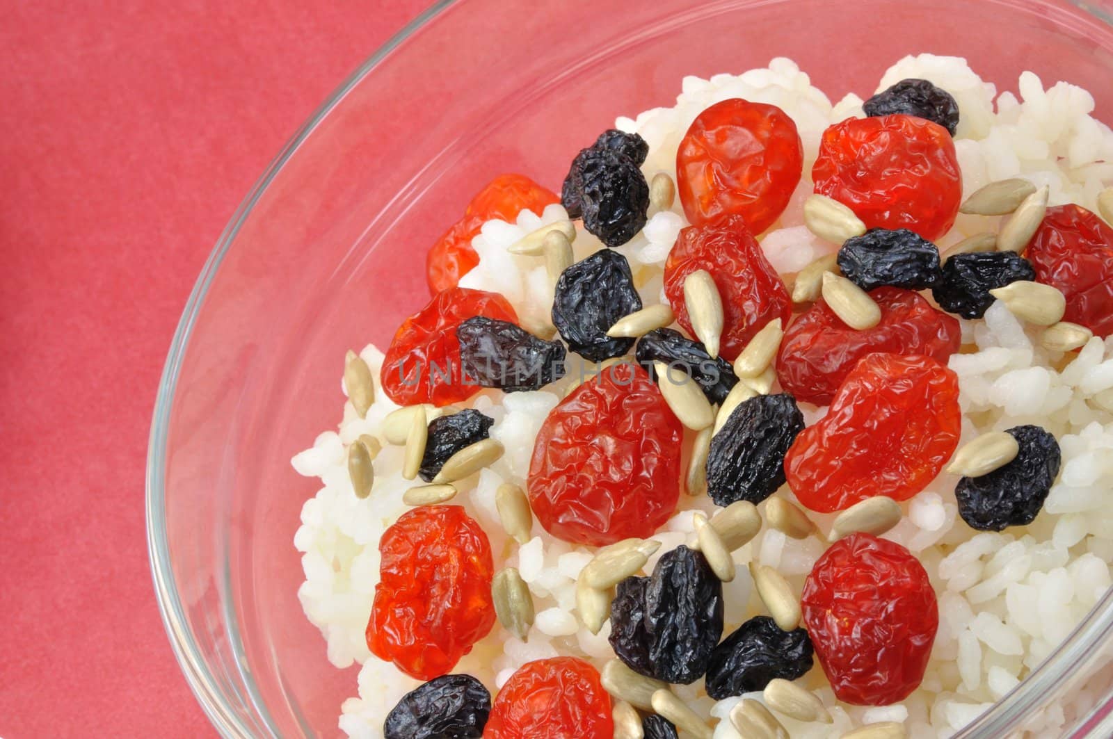 Boiled White Rice with Dried Fruit and Sunflower Seeds in Transparent Bowl on Red Background