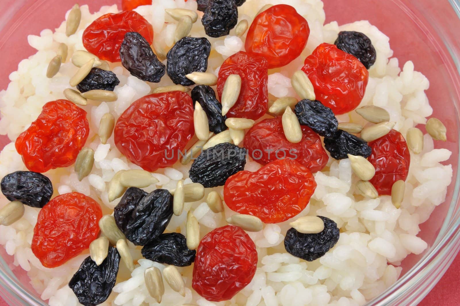 Boiled White Rice with Dried Fruit and Sunflower Seeds in Transparent Bowl on Red Background