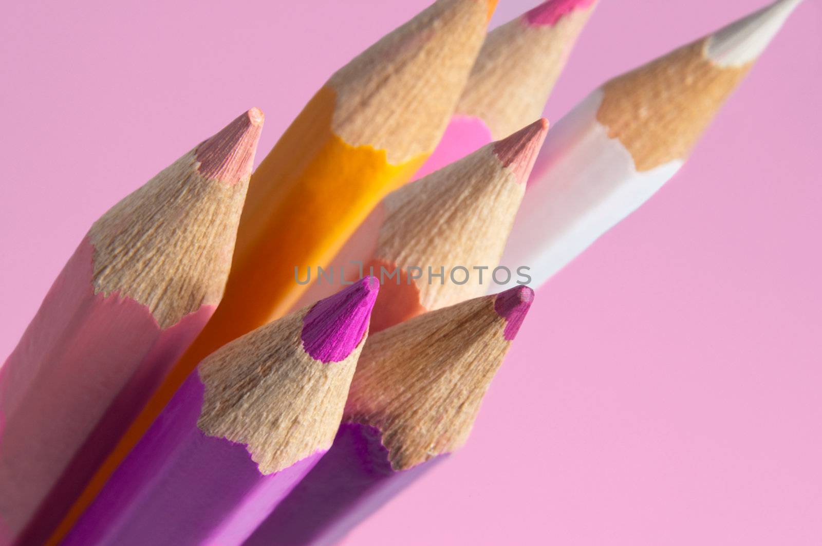 Close up capturing the tops of a small group of pastel coloured drawing pencils arranged over pink.