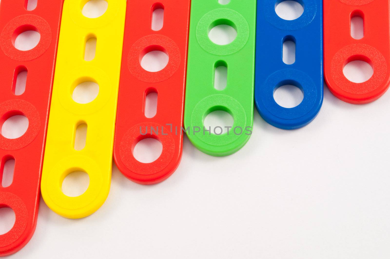 Close up capturing components from a brightly coloured child's construction set arranged over white.