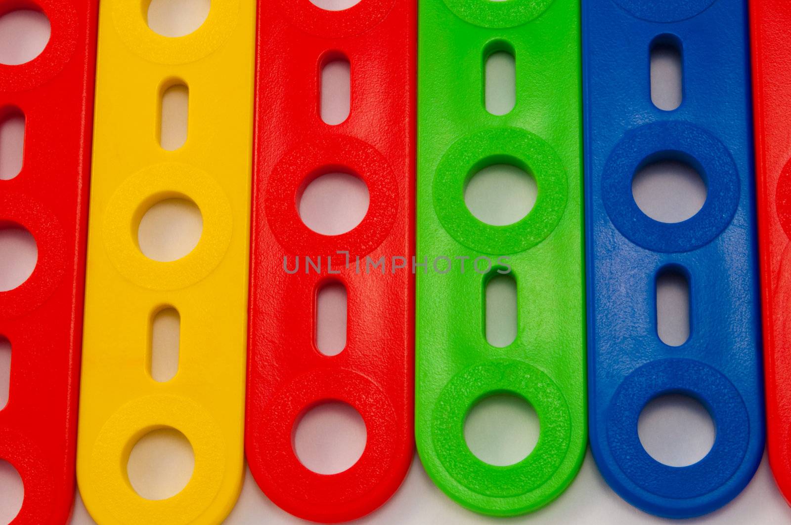 Close up capturing components from a brightly coloured child's construction set arranged over white.