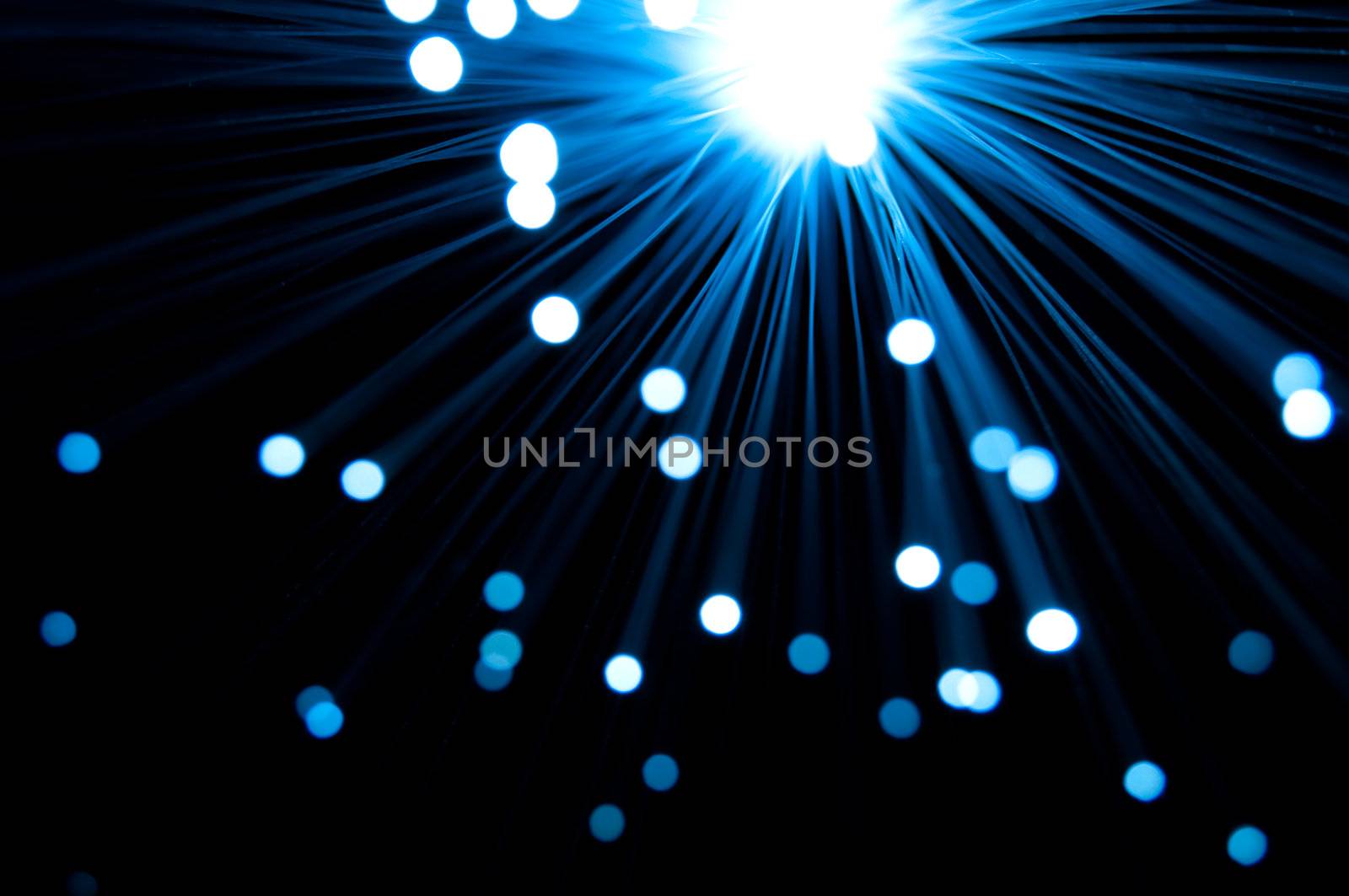Close and abstract style capturing the ends of many blue fibre optic light strands emitted from a central light source against black.