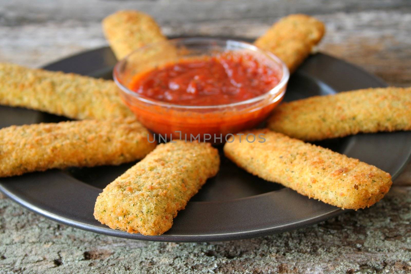 Mozzarella cheese sticks on a plate with marinara sauce.  Used a shallow depth of field on the front stick.