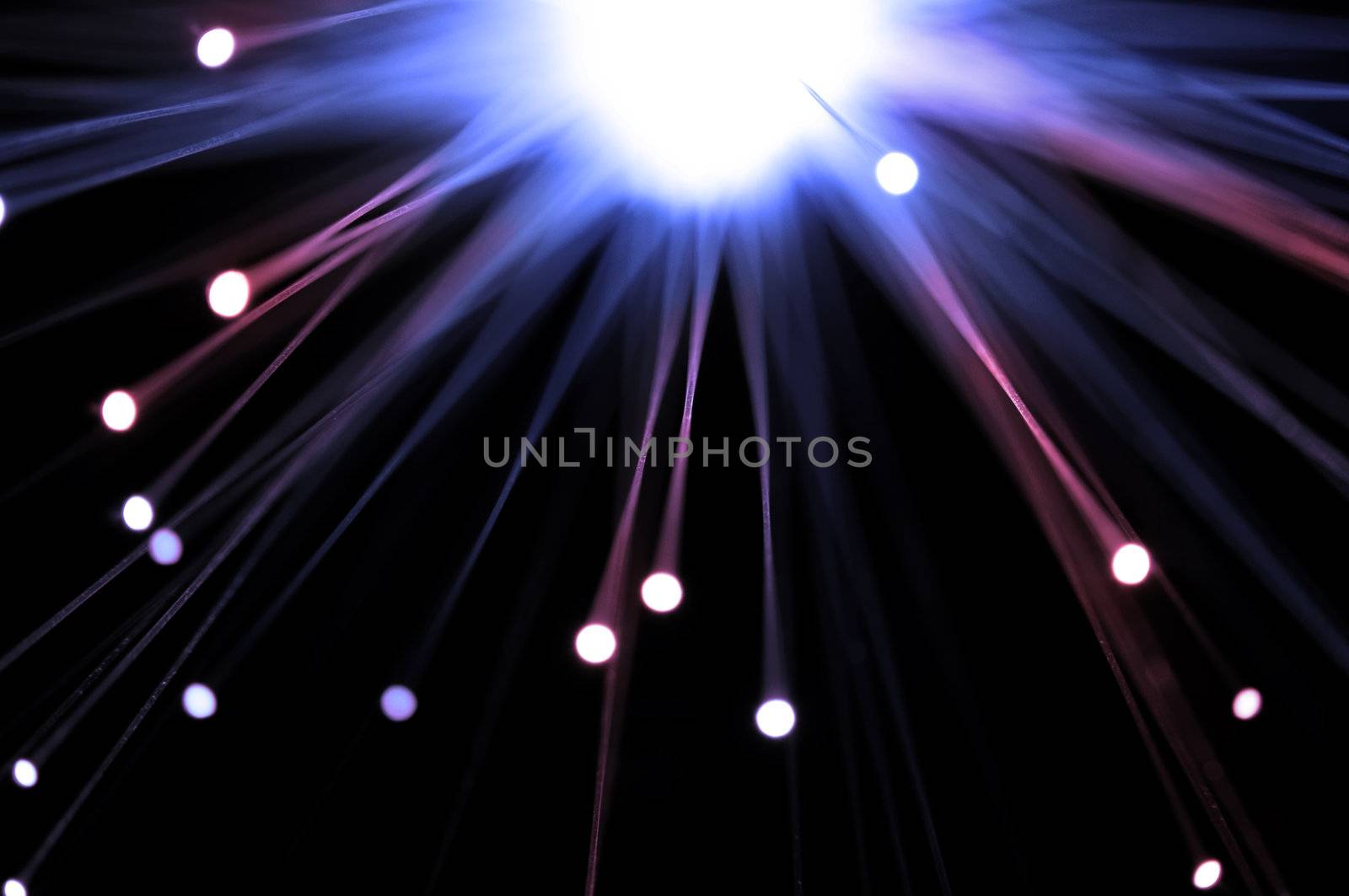 Close up and abstract style capturing the ends of many illuminated fibre optic light strands emitted from a central white light against dark background.