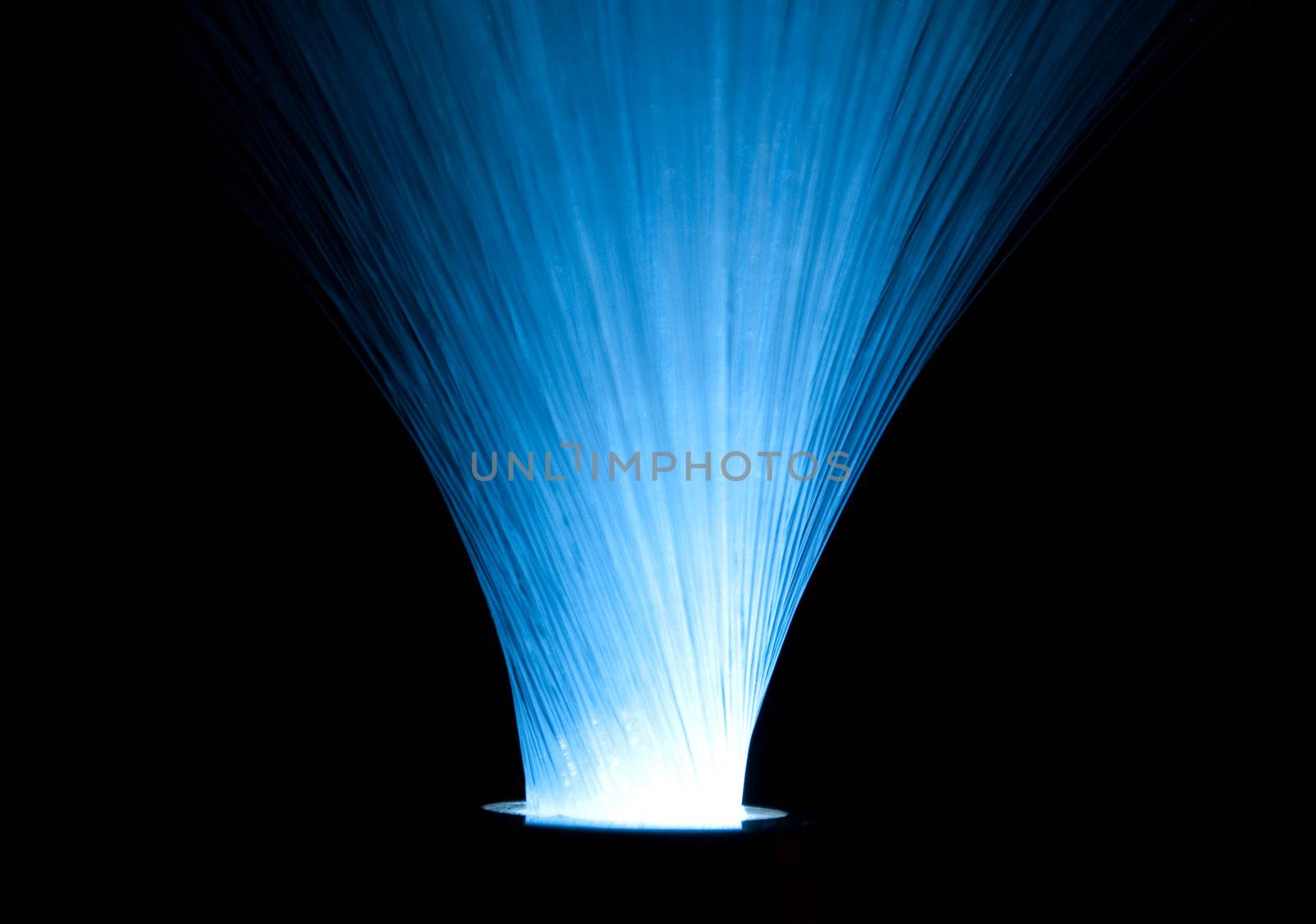 Close up and low level capturing many fibre optic light strands emitted from a central light source against a black background.