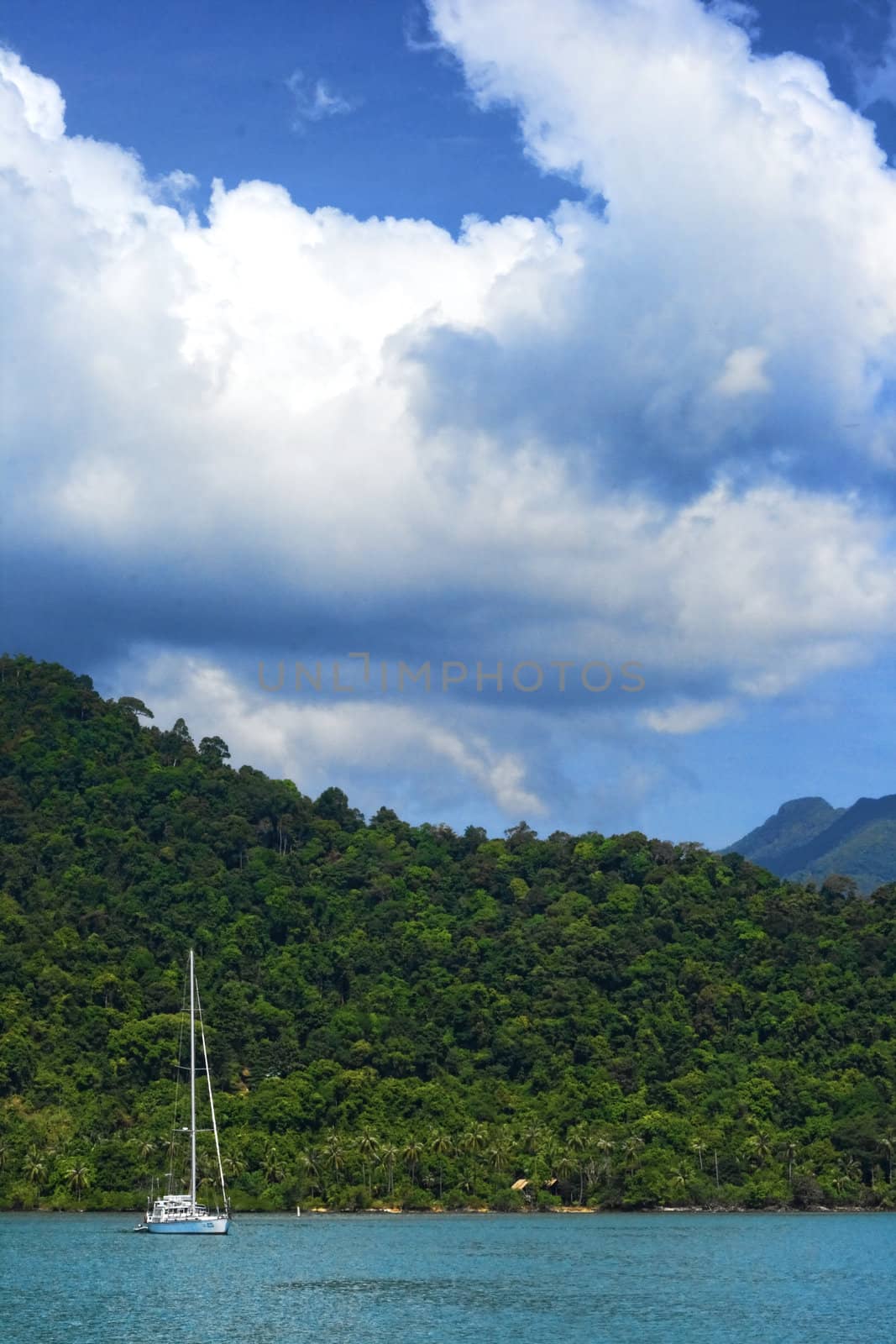 Sailboat off the coast of tropical island in blue water with clouds above