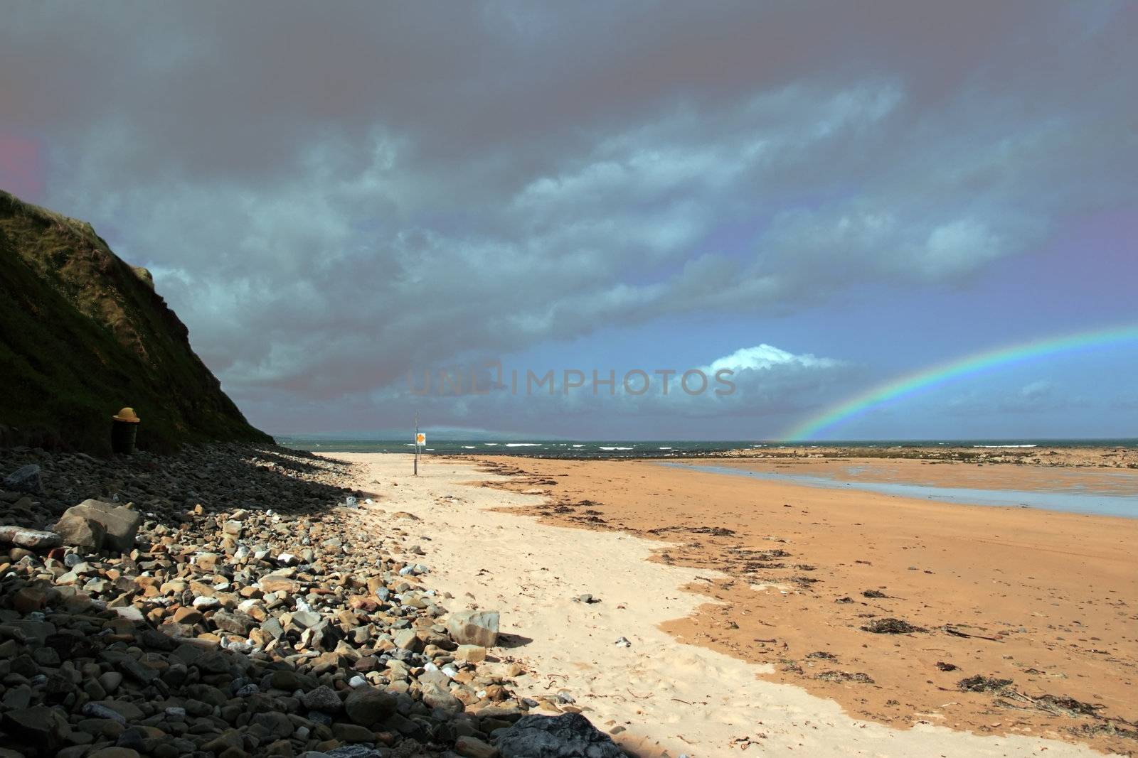 a rocky beach on a warm wet day with a calm sea and a rainbow after a shower an ideal place to have a walk in ireland